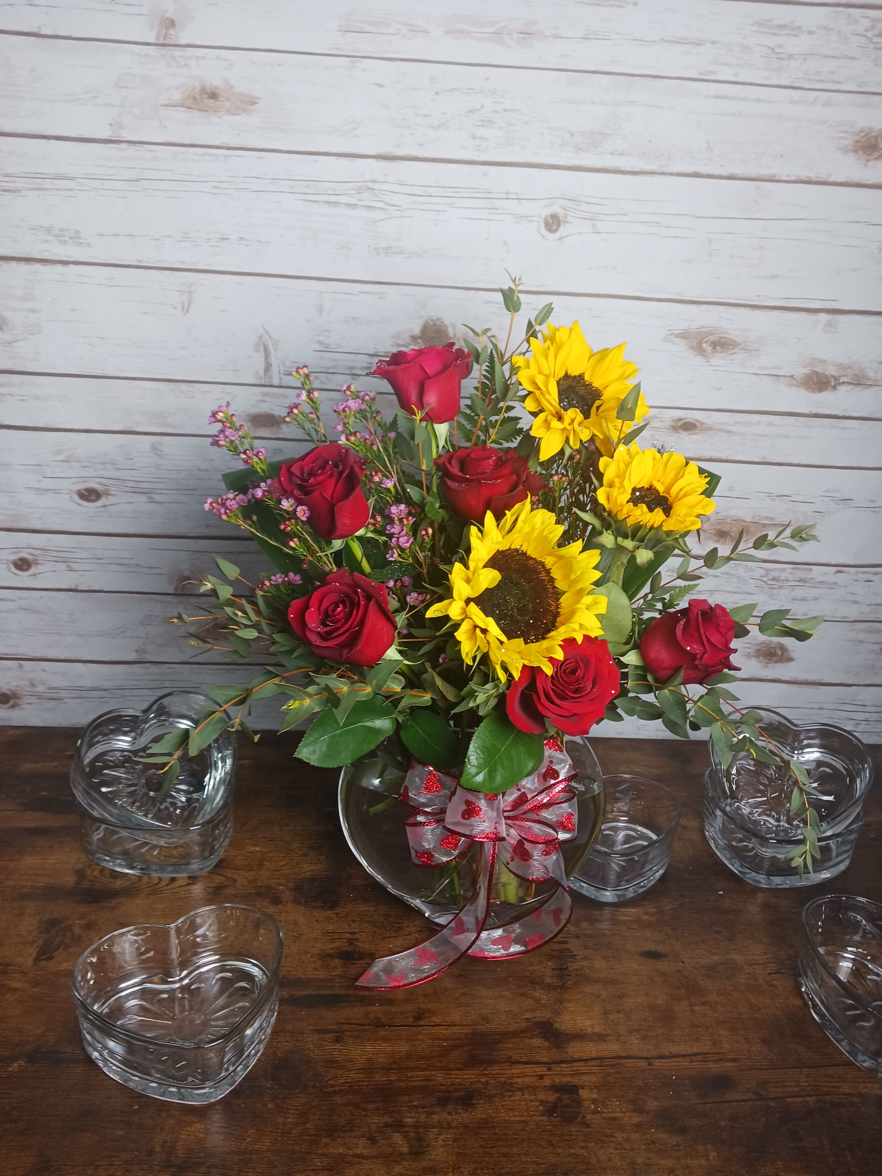 Bouquet of red roses and yellow sunflowers in a glass vase with ribbon
