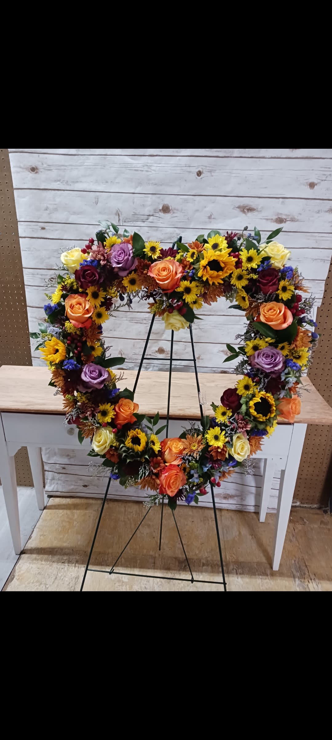 Heart-shaped floral wreath on a metal stand with roses and sunflowers