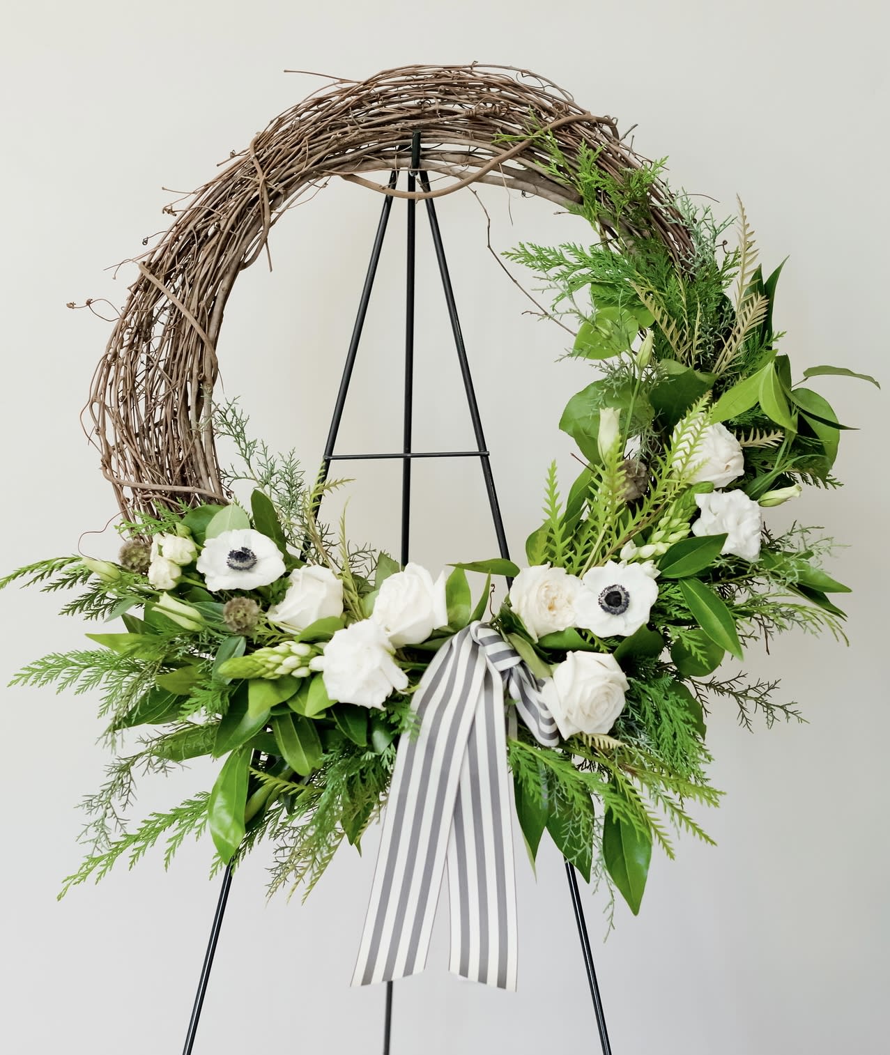 37 | Vigne Chevalet Fleurs - grapevine standing easel - Grapevine wreath funeral standing spray. Includes seasonal blooms and foliage on an easel with a striped ribbon. Can specify colors you'd like included in the special instructions.
