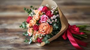 Bouquet of pink, peach, and red roses wrapped in brown paper with a red ribbon