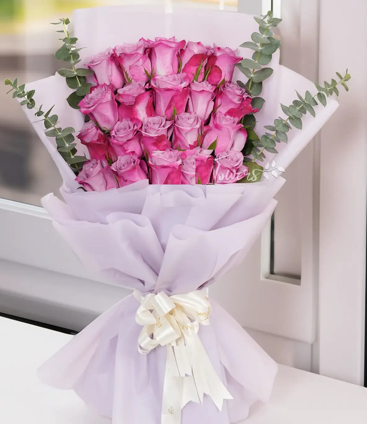 Bouquet of pink roses wrapped in pale lavender paper with eucalyptus accents