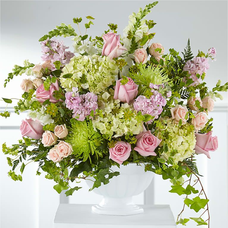 Pink roses and pale green hydrangeas in a white pedestal vase