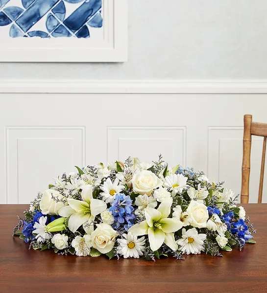 Low floral centerpiece with white lilies, roses, and daisies on a table
