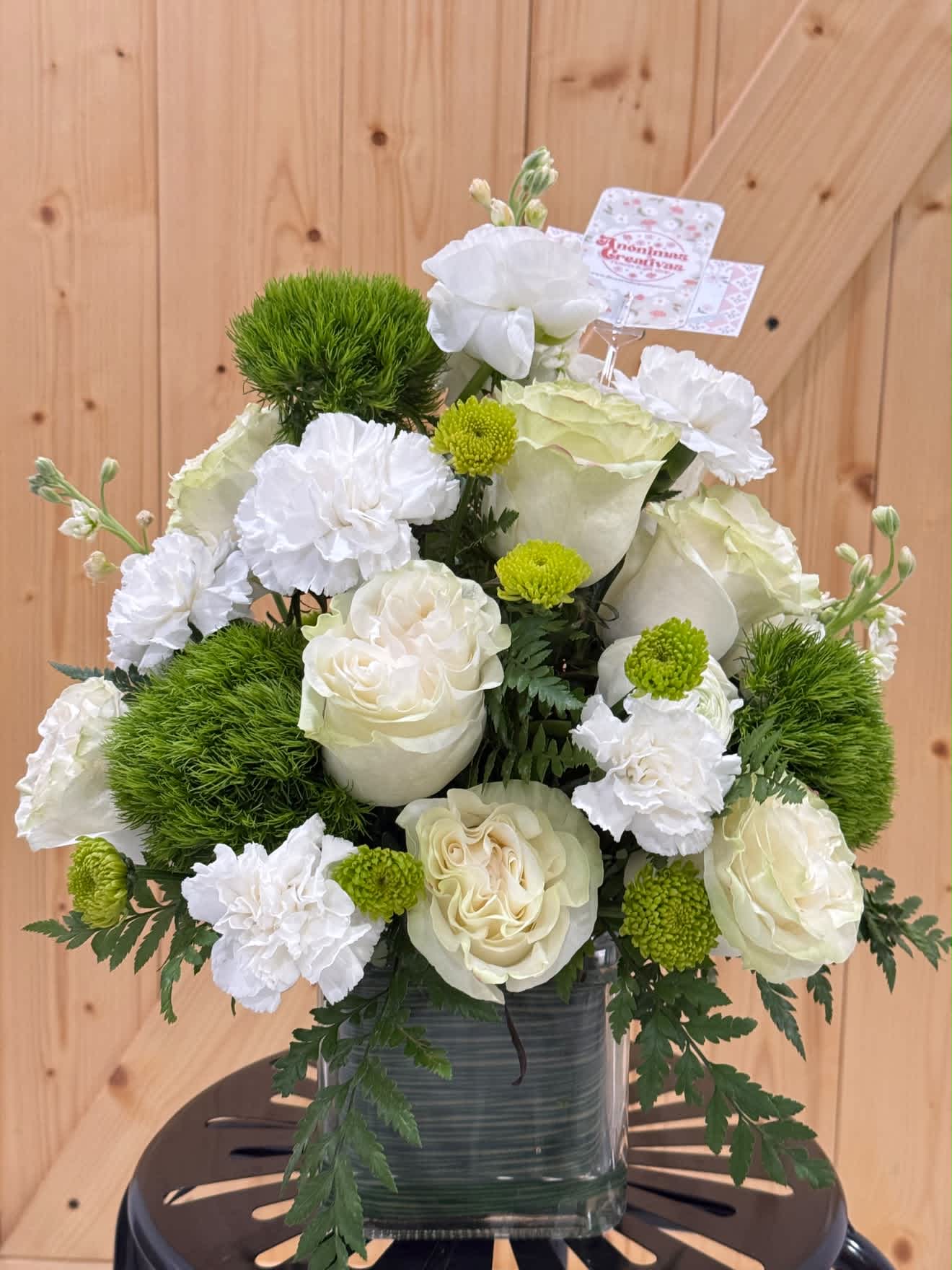 White roses and carnations in a glass vase with green pom-pom accents