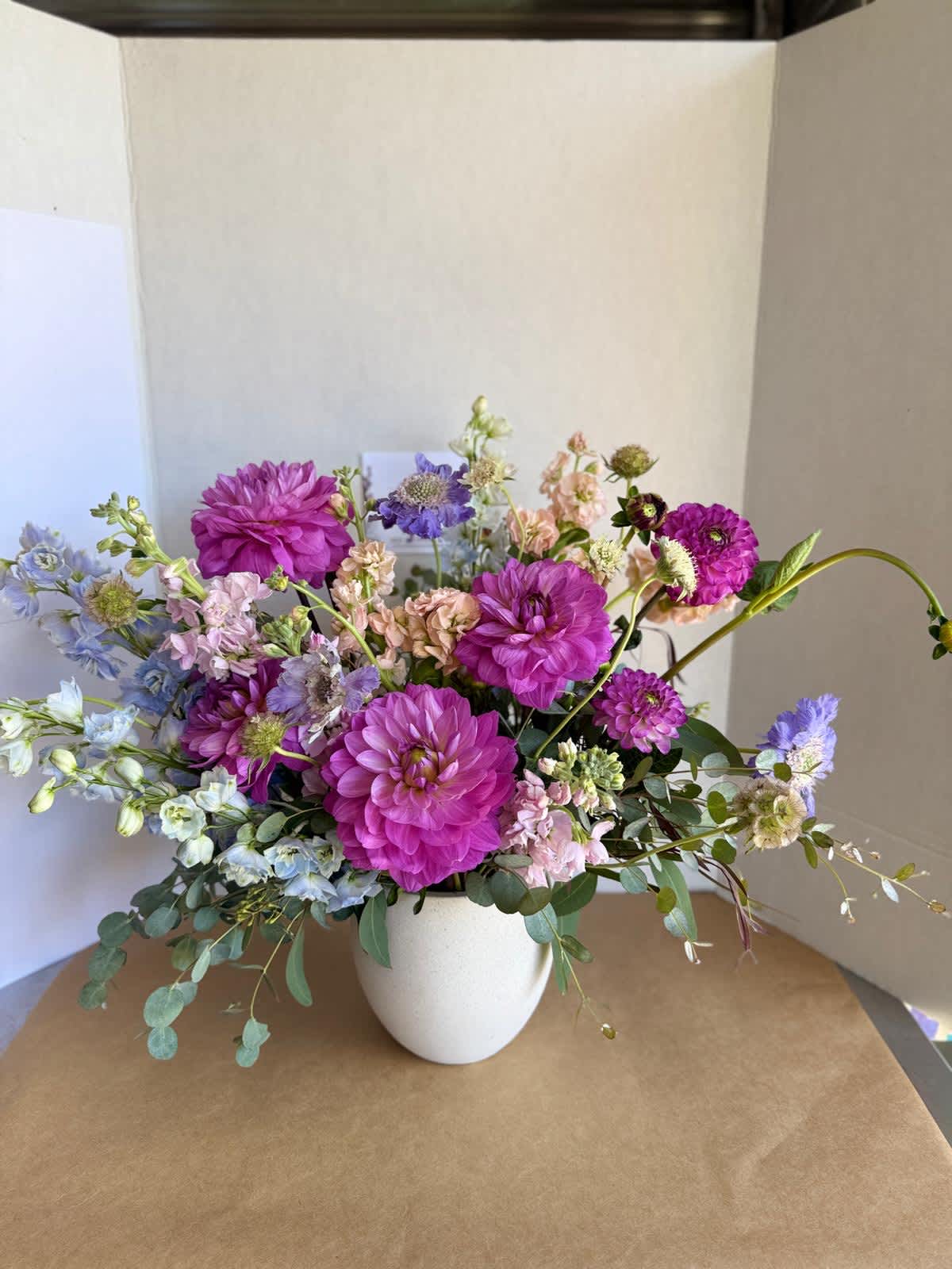 Mixed bouquet of purple, pink, and blue flowers in a white vase