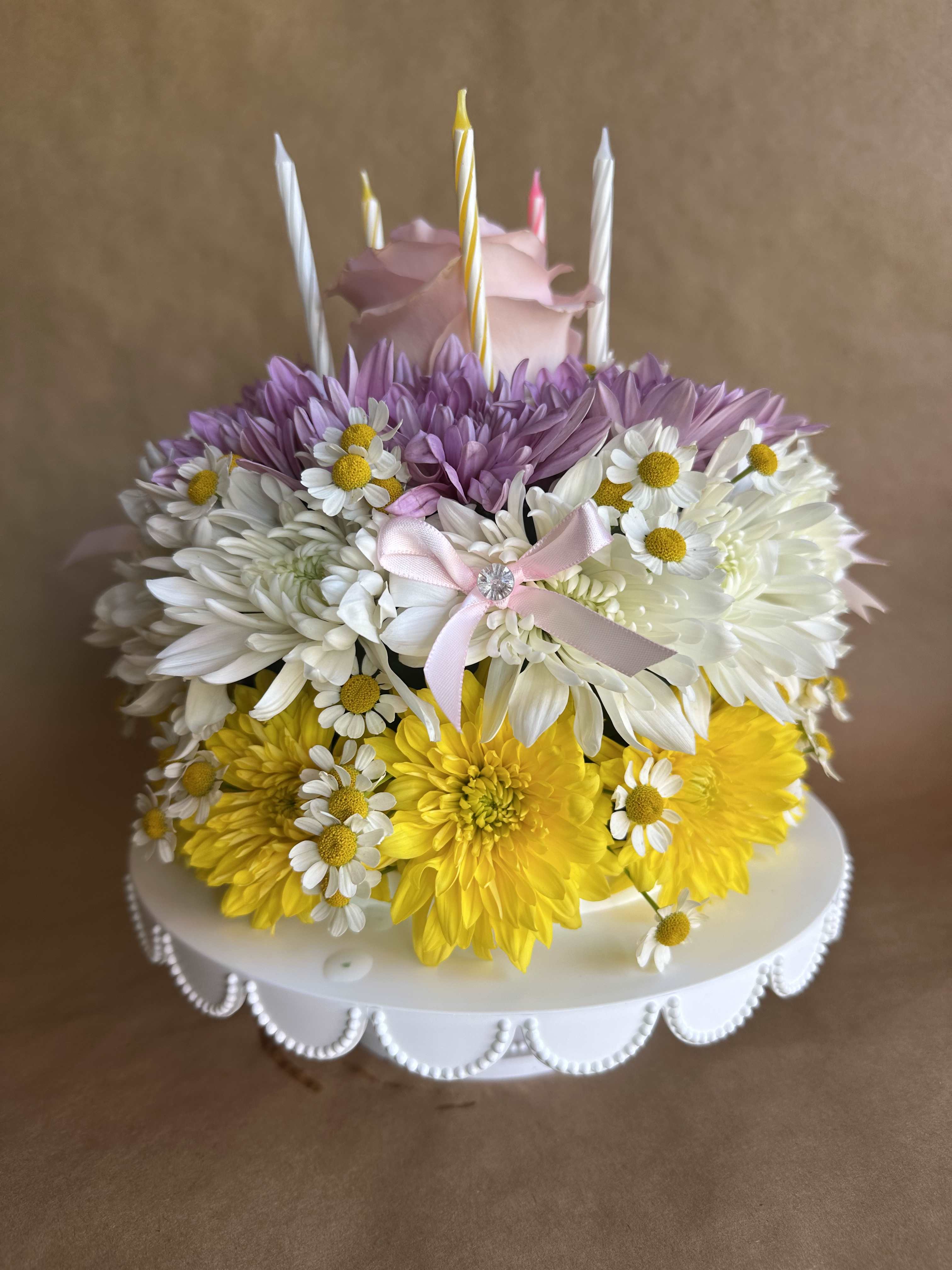 Flower-covered cake with candles and a pink rose topper