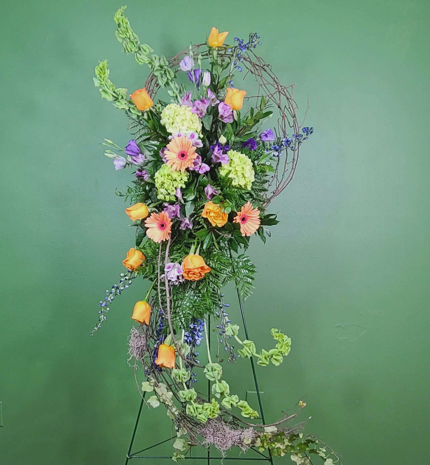Tall floral arrangement with orange roses, gerbera daisies, and purple blooms