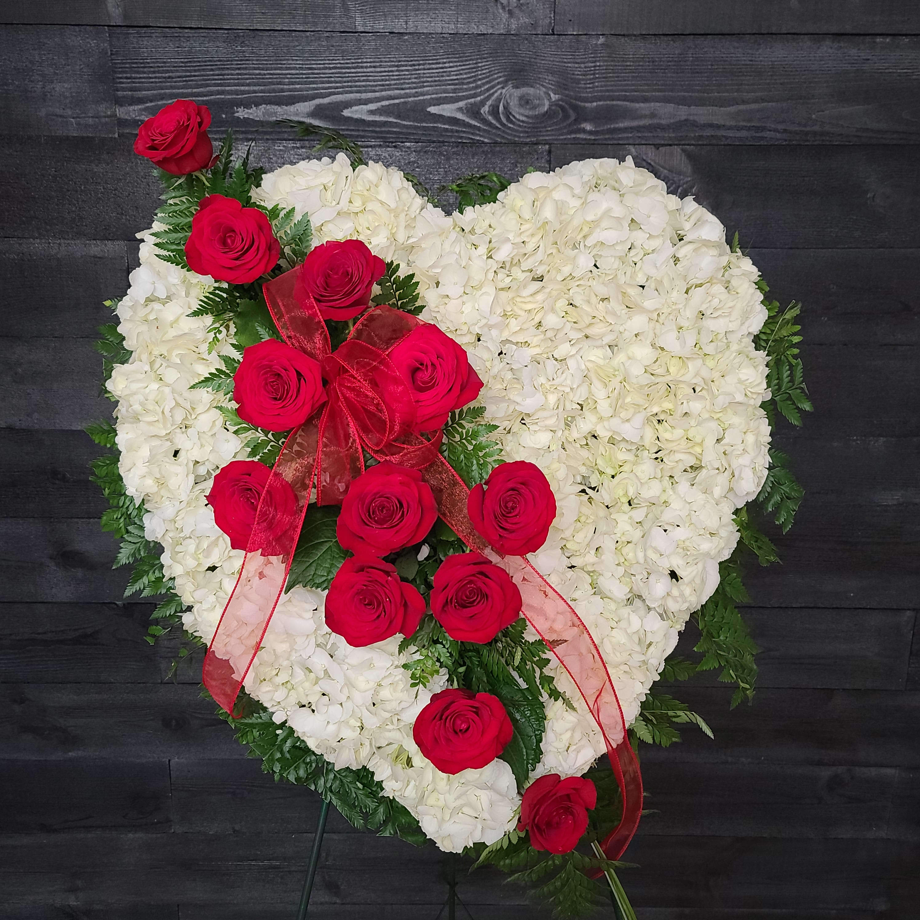 Heart-shaped white floral arrangement with red roses and a red ribbon