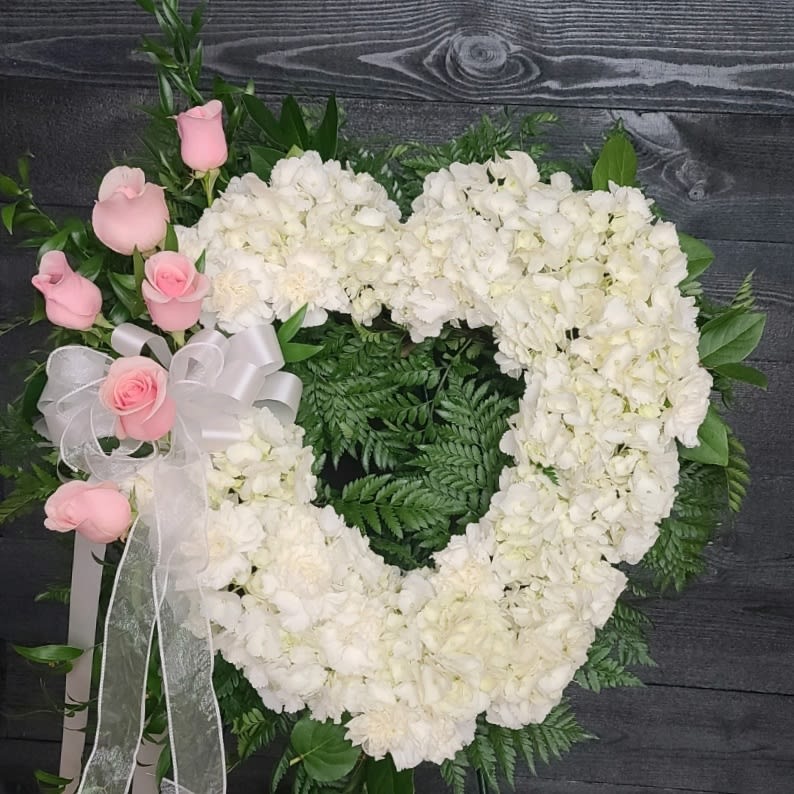 Heart-shaped white floral wreath with pink roses and a white ribbon bow