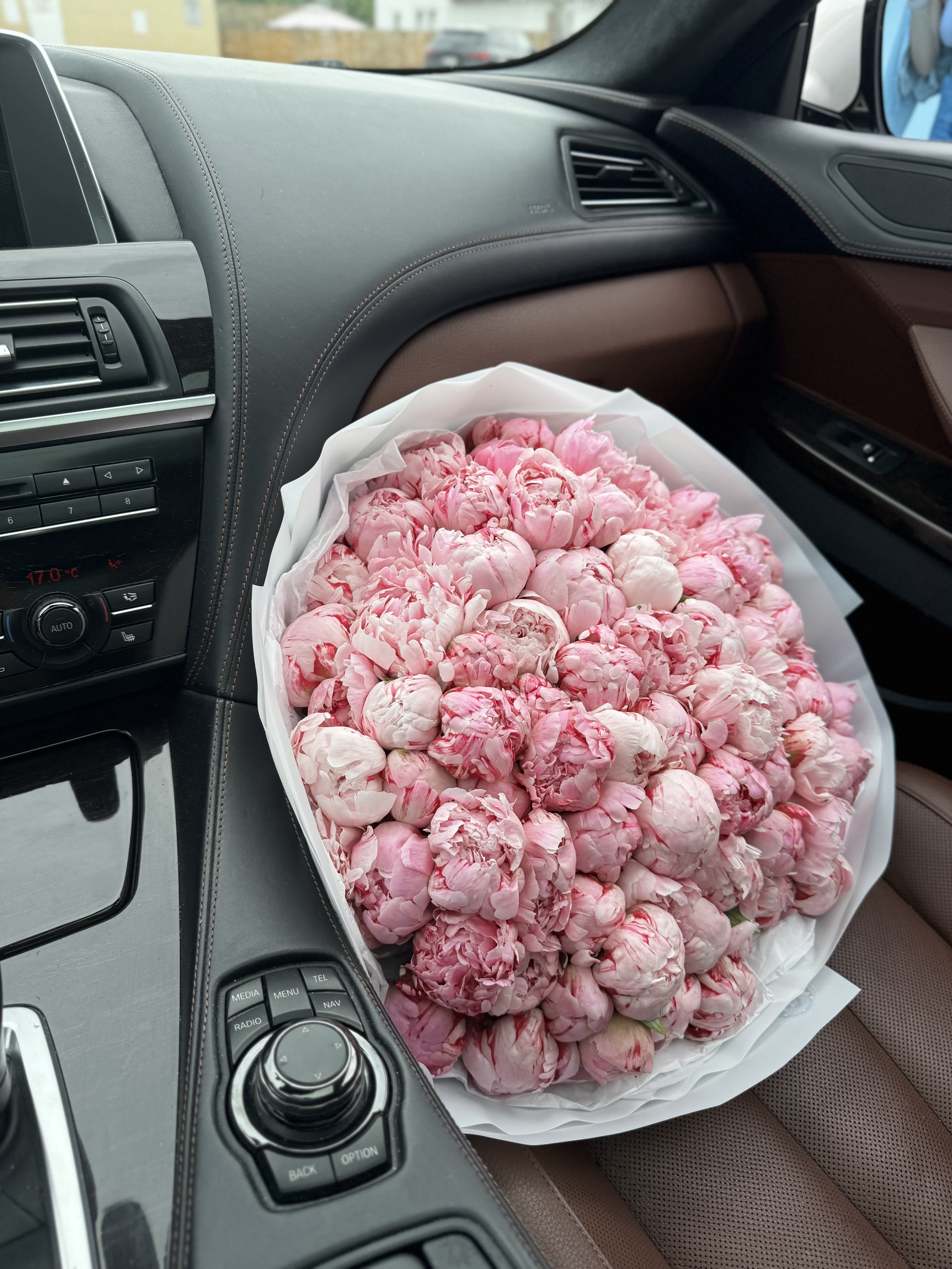 Large bouquet of pink peonies wrapped in white paper on a car seat
