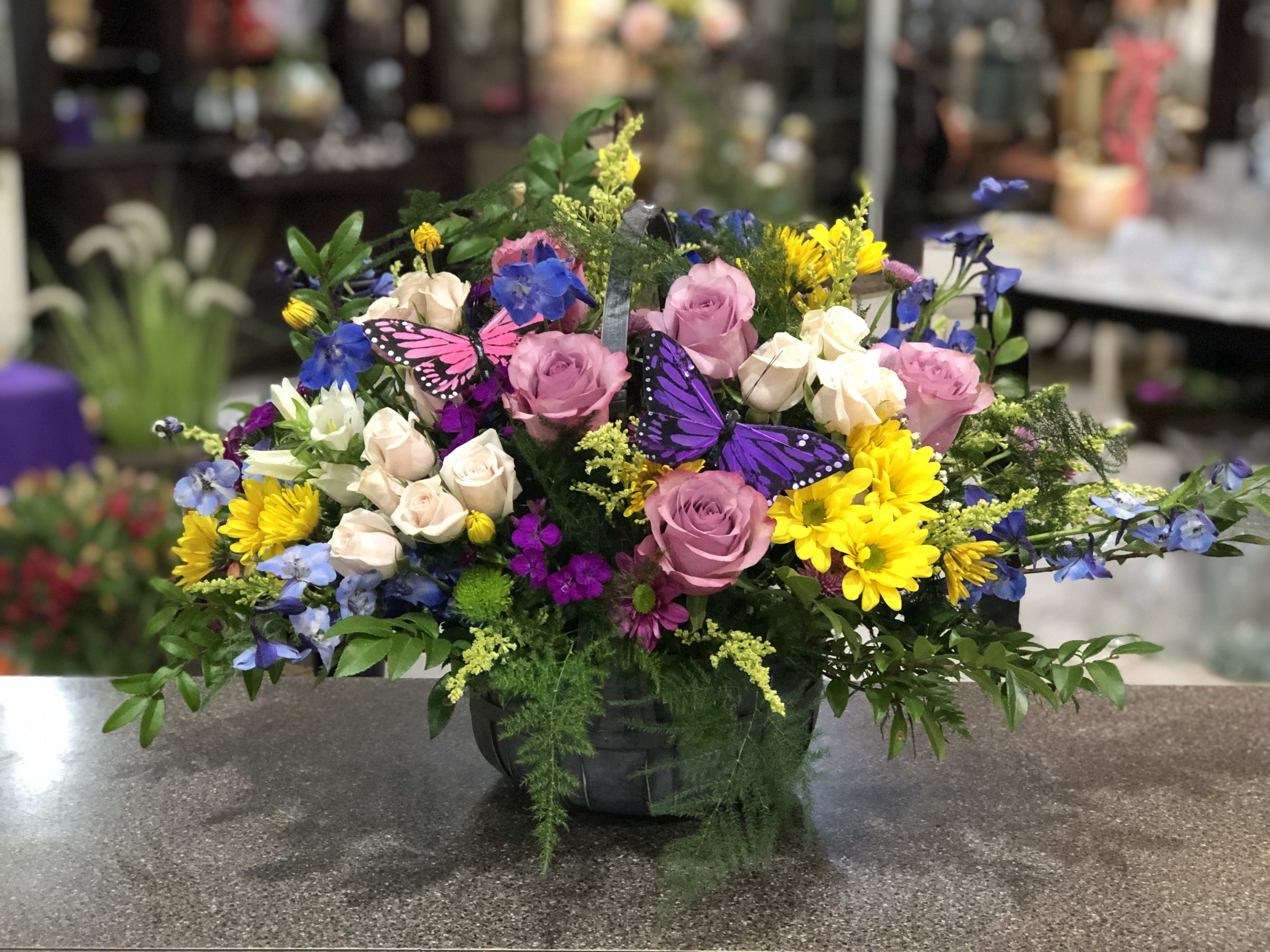 Mixed bouquet of pink roses, yellow daisies, and blue flowers in a black basket