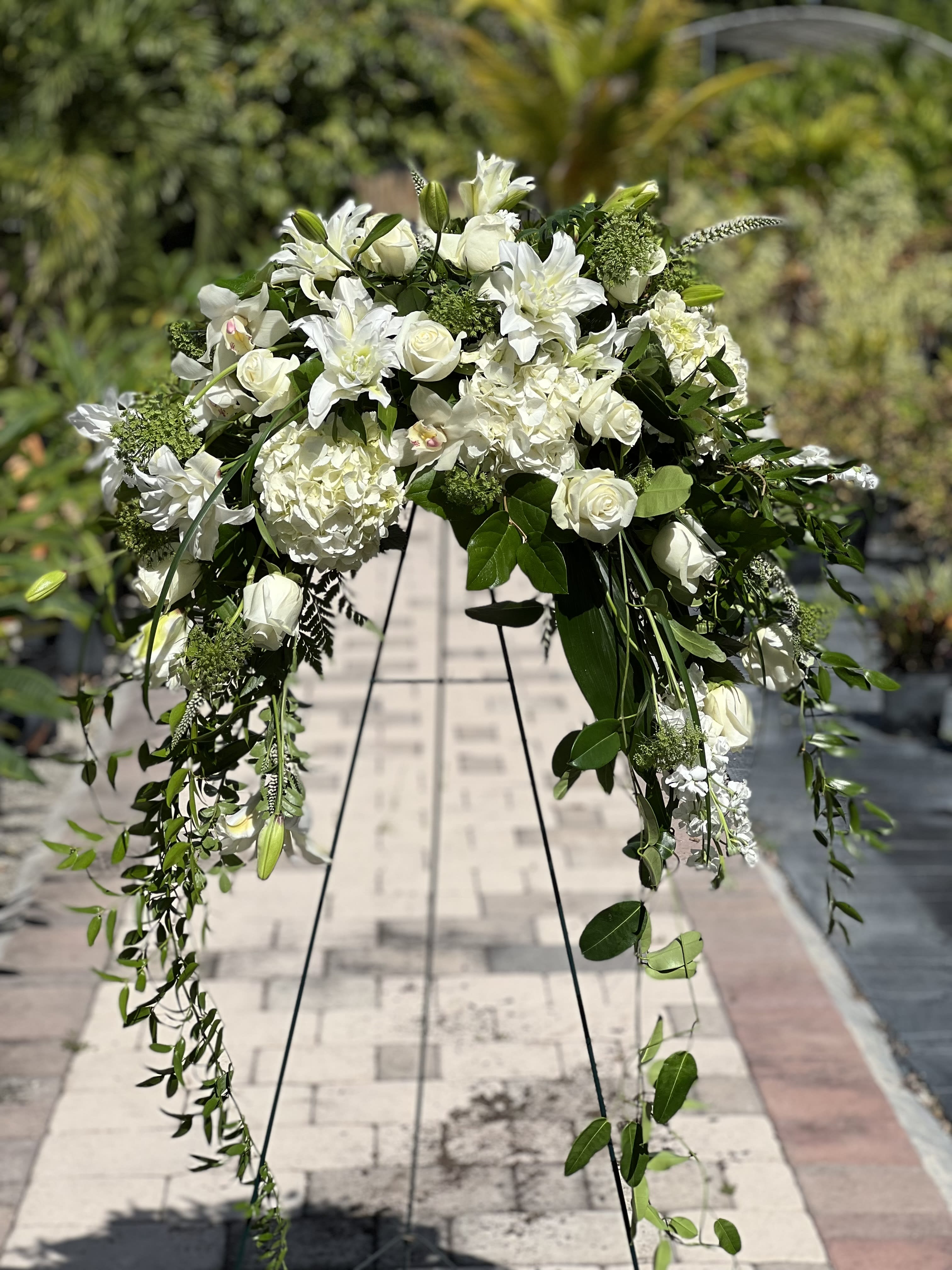 White floral spray on a black stand with trailing greenery