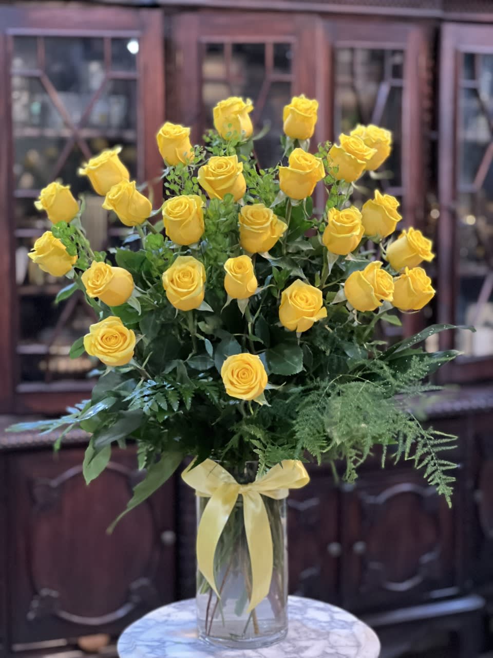 Yellow roses arranged in a clear glass vase with a ribbon