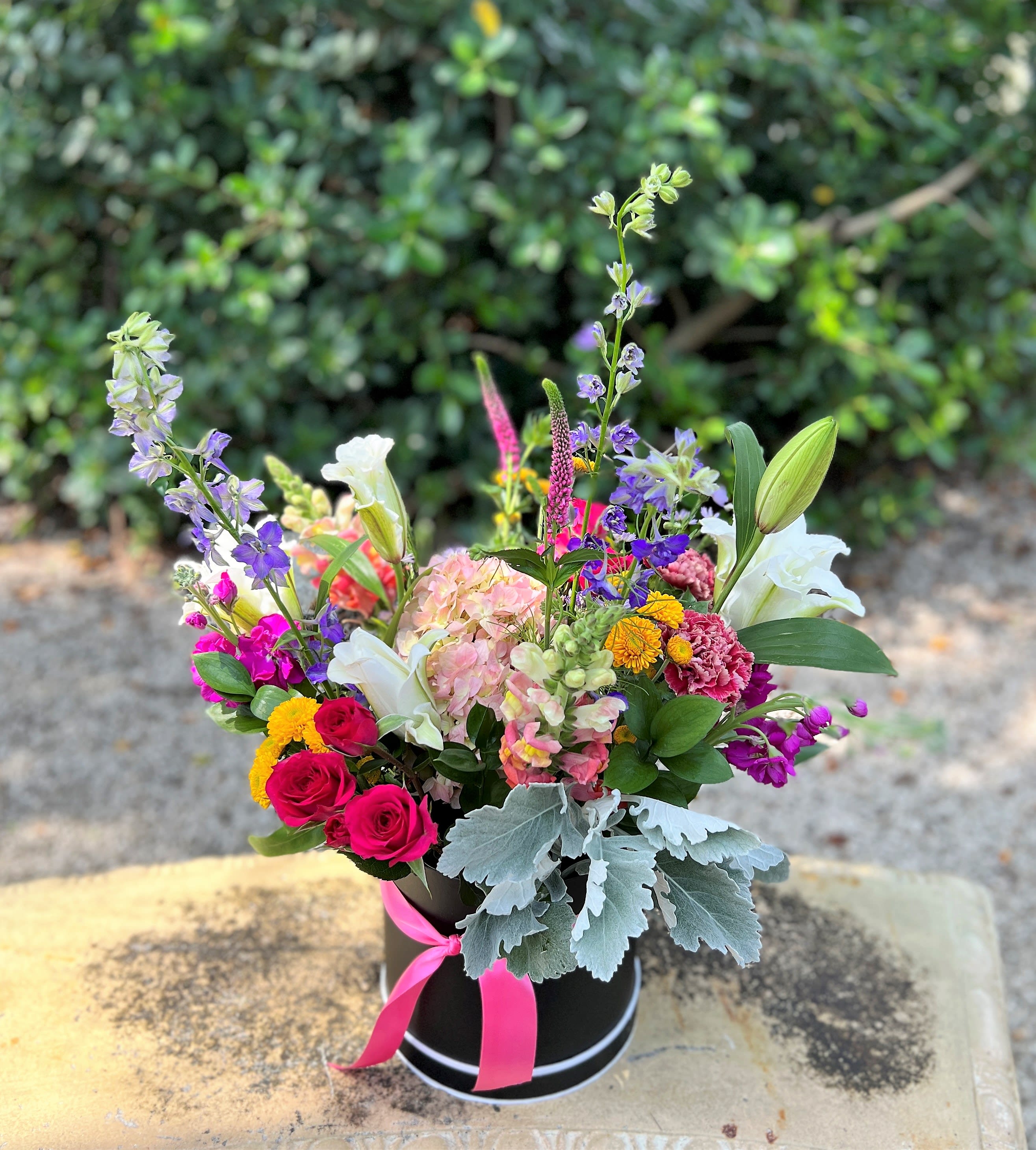 Colorful mixed flower arrangement in a black hatbox with a pink ribbon