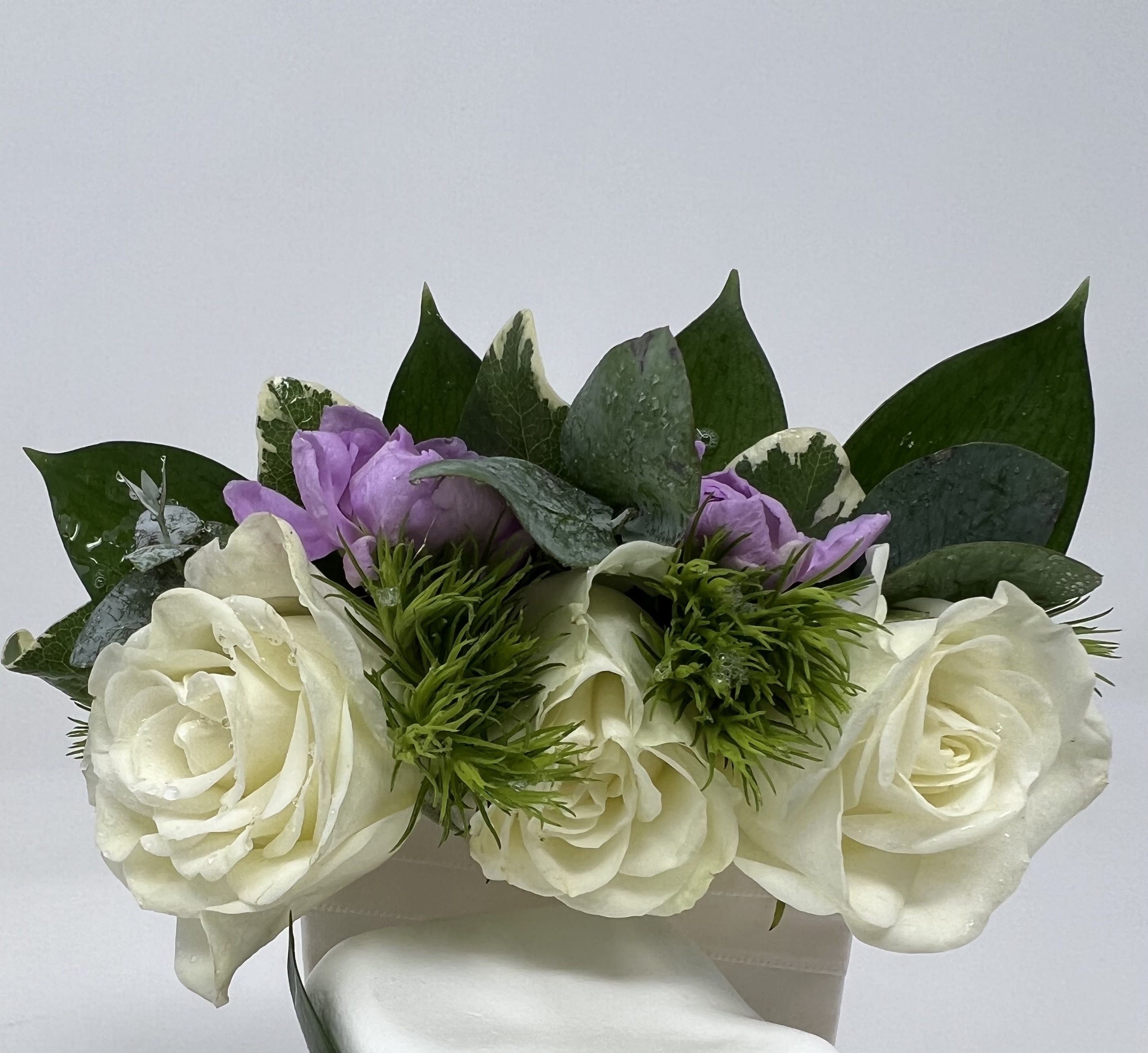 White roses with purple blooms and greenery in a white box
