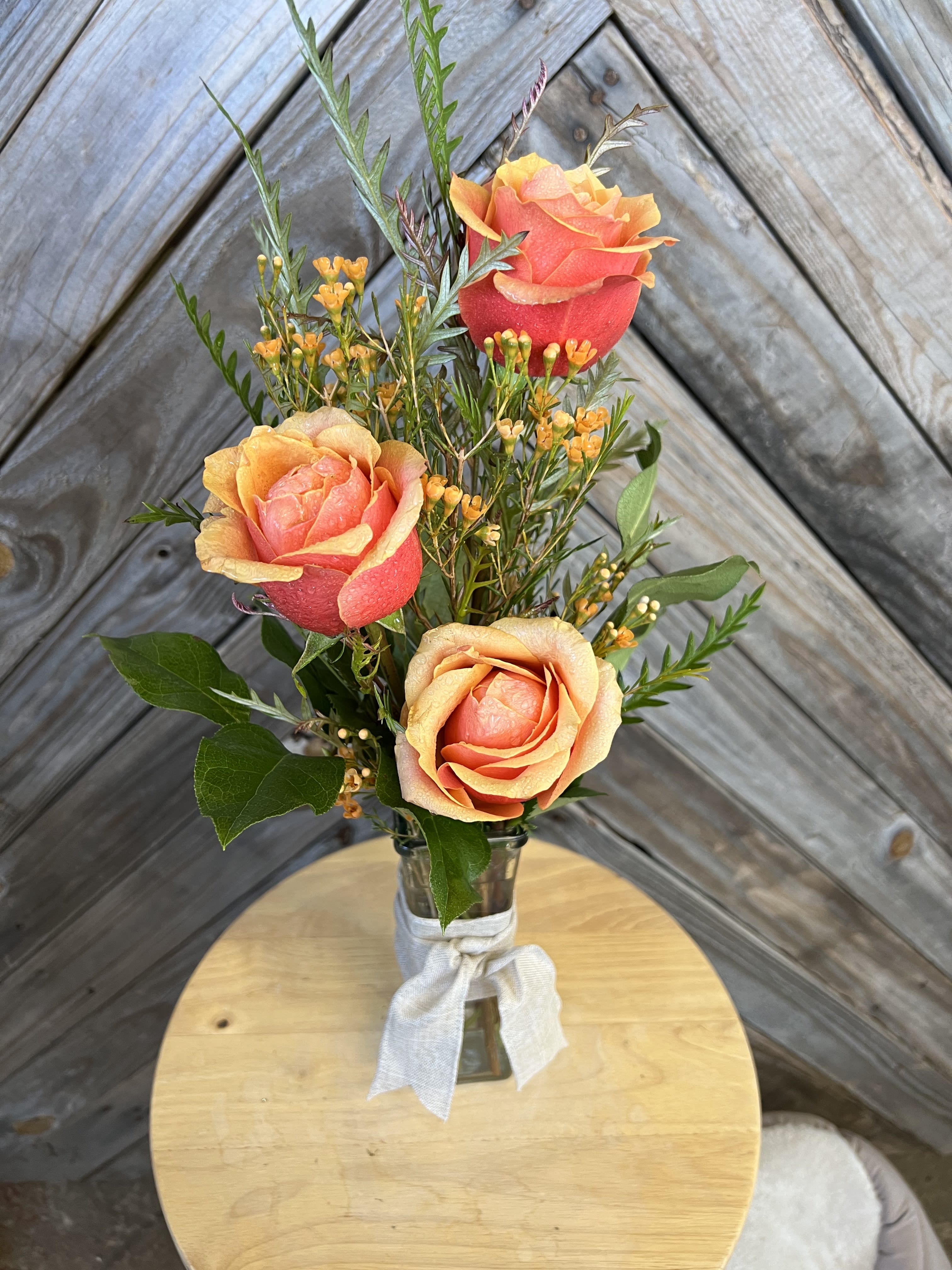 Three coral roses in a small glass vase with a white ribbon