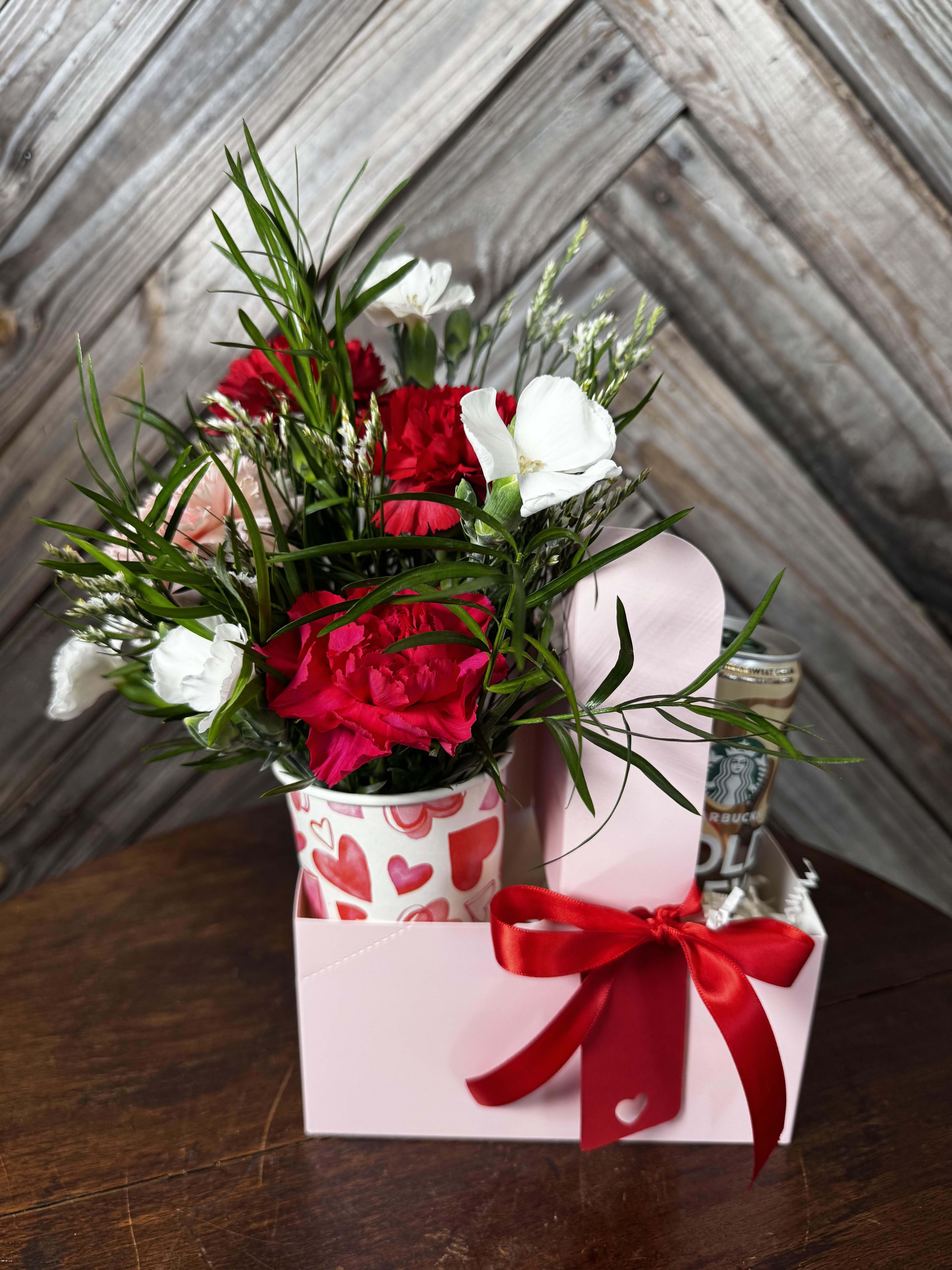 Red and white carnations in a heart-patterned cup with a gift box and ribbon