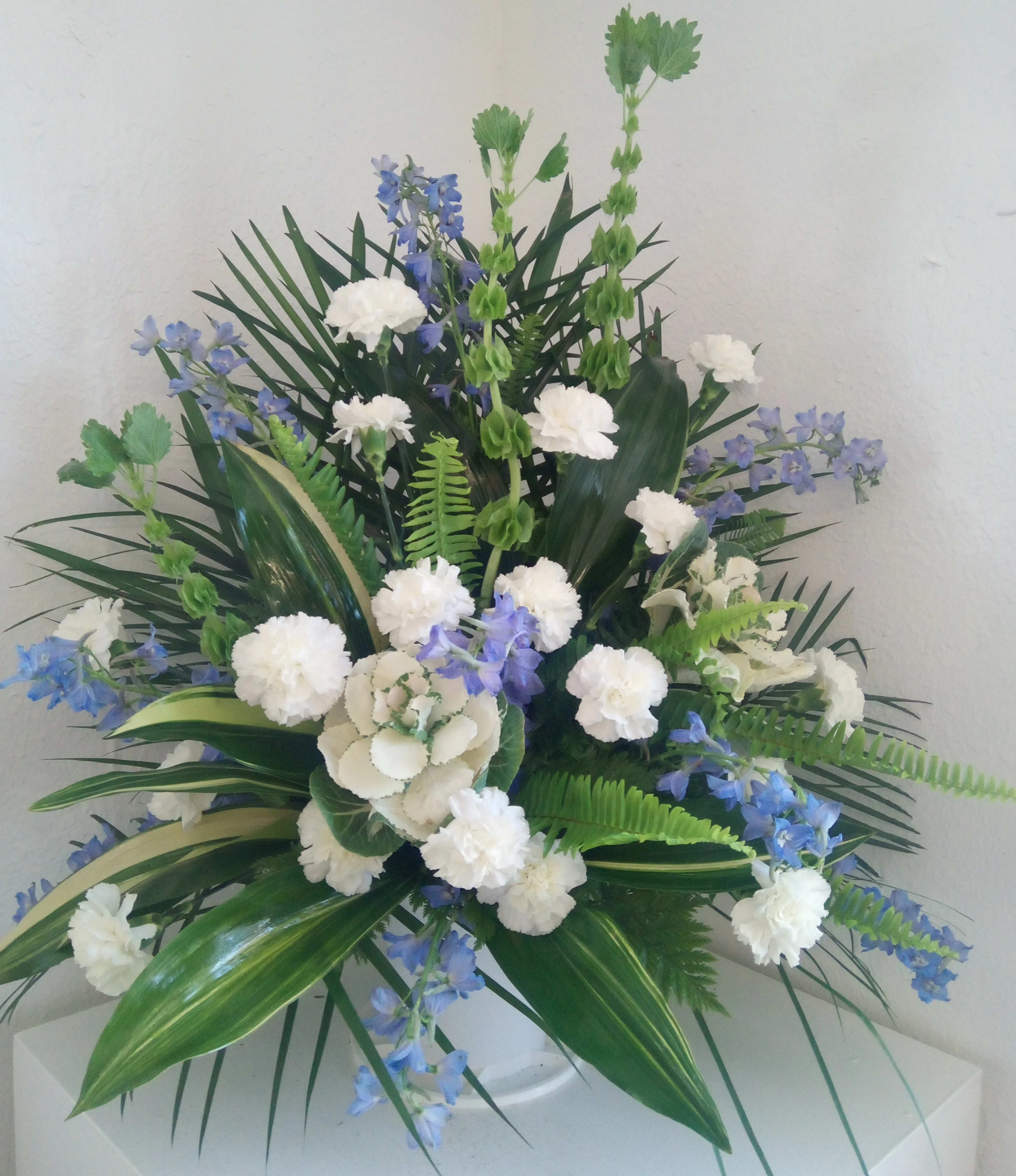White carnations and blue flowers in a white vase with tropical foliage