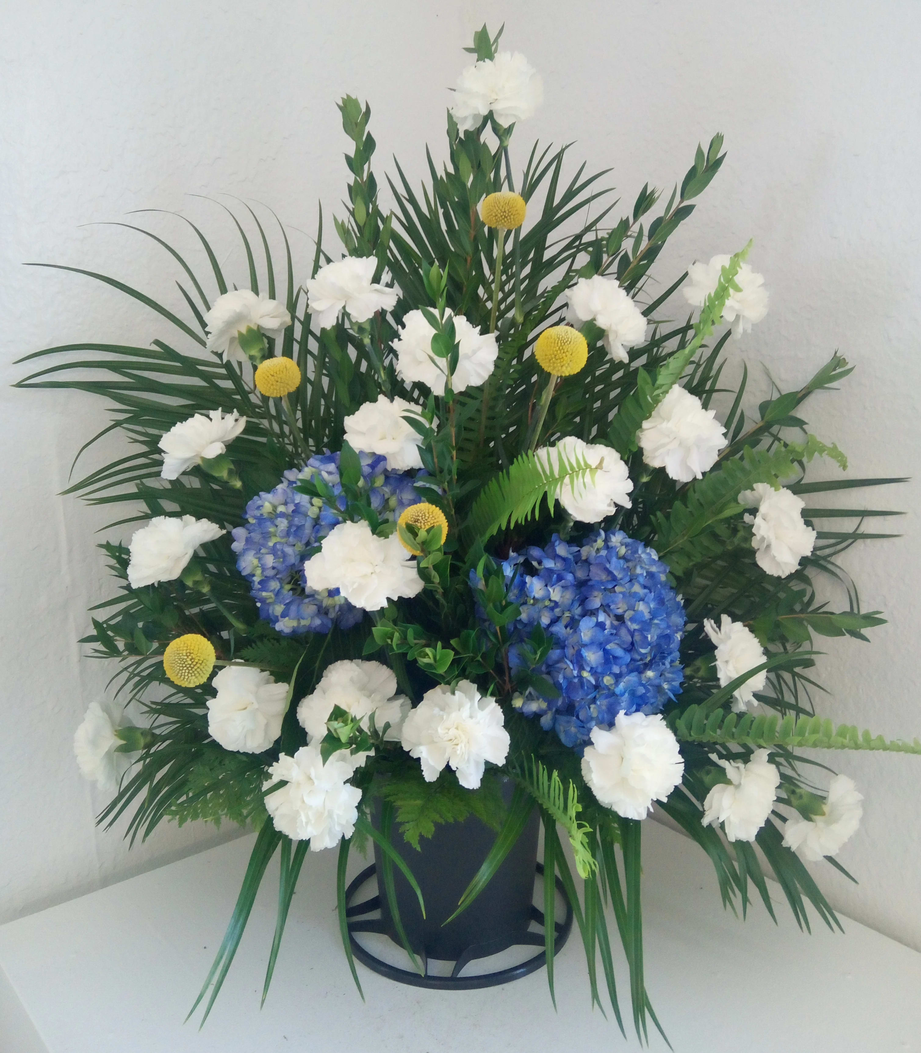 Blue hydrangeas and white carnations in a black pot with palm foliage