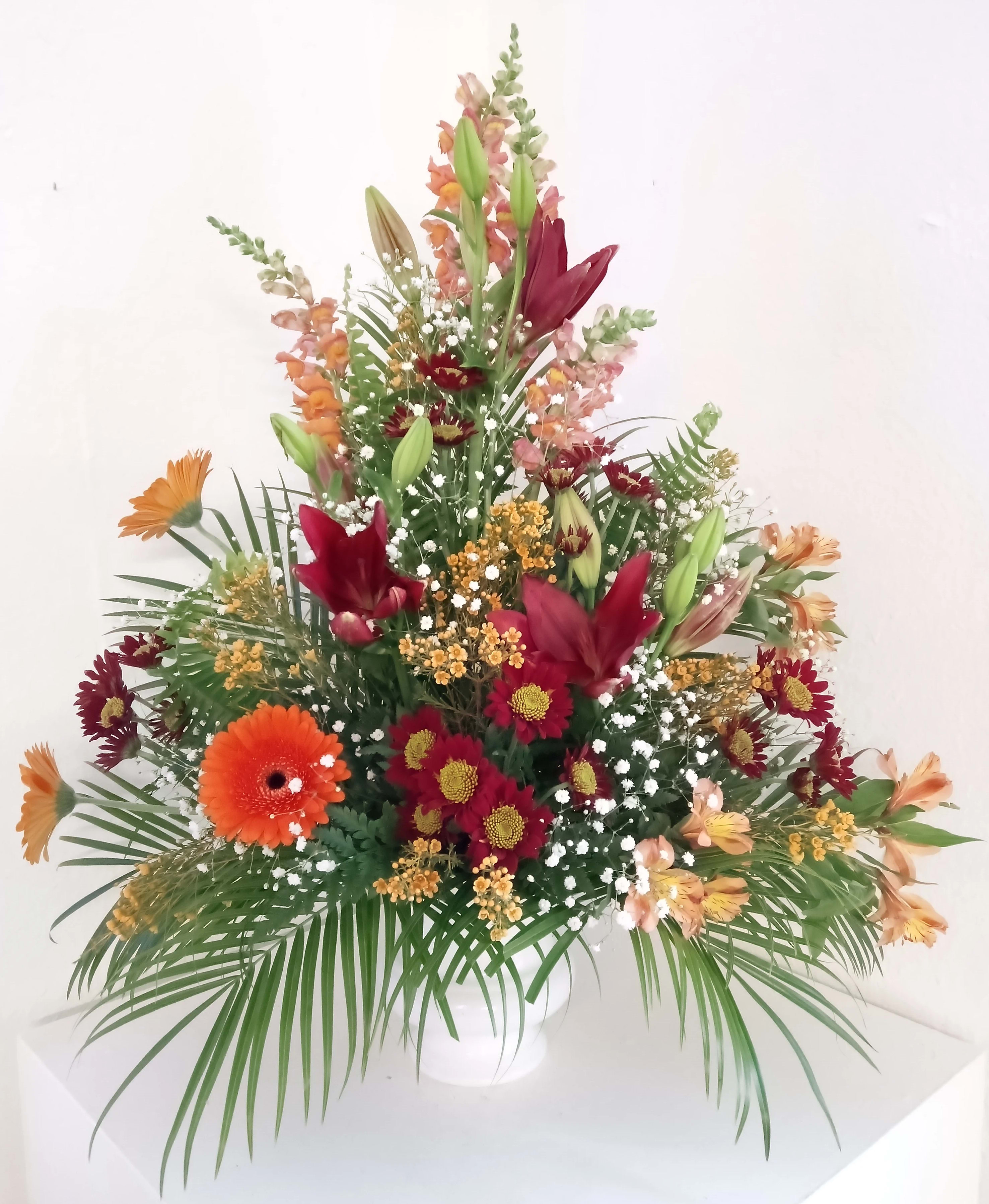 Tall mixed floral arrangement in a white vase with orange and burgundy blooms