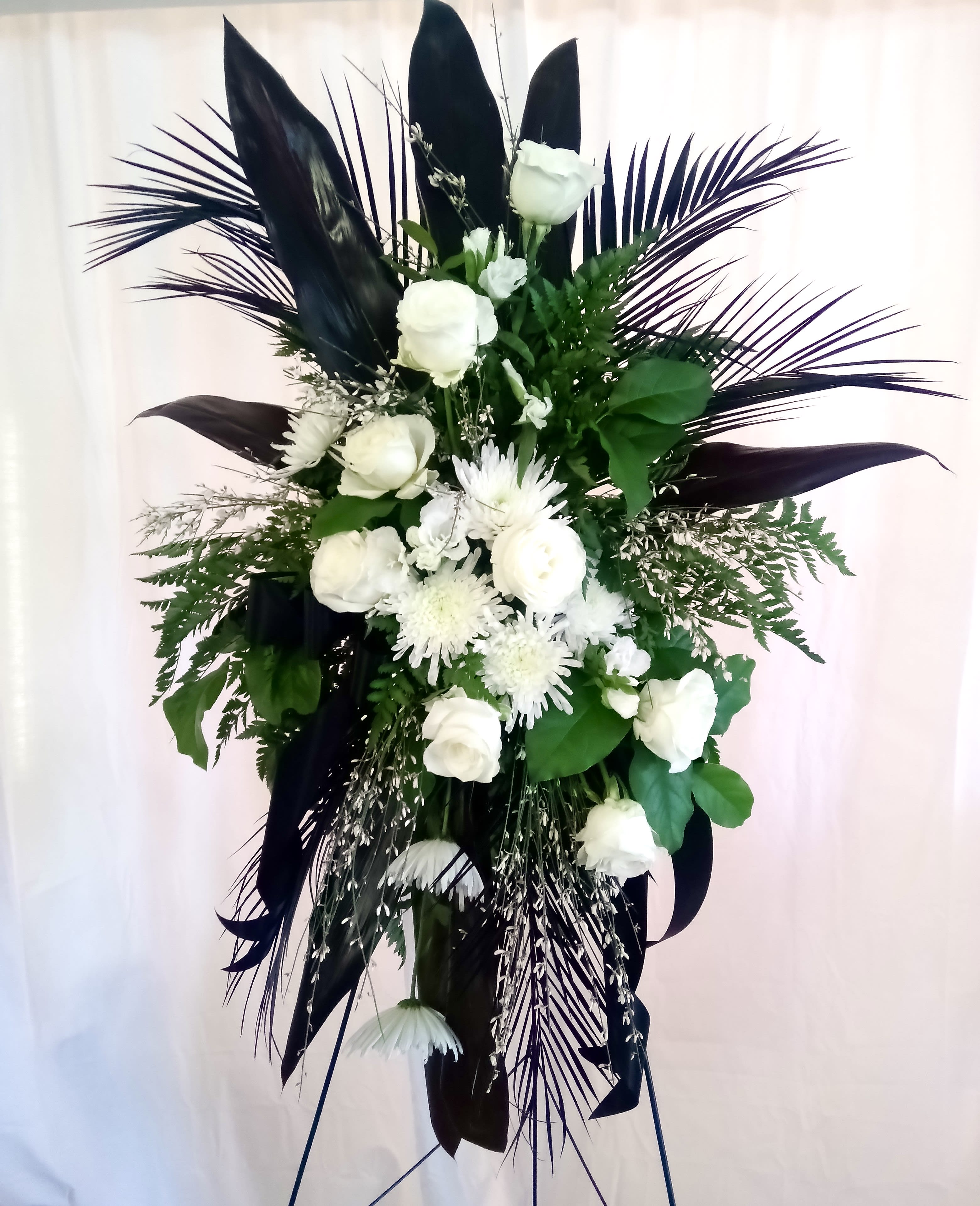 White floral standing spray with dark foliage on a stand