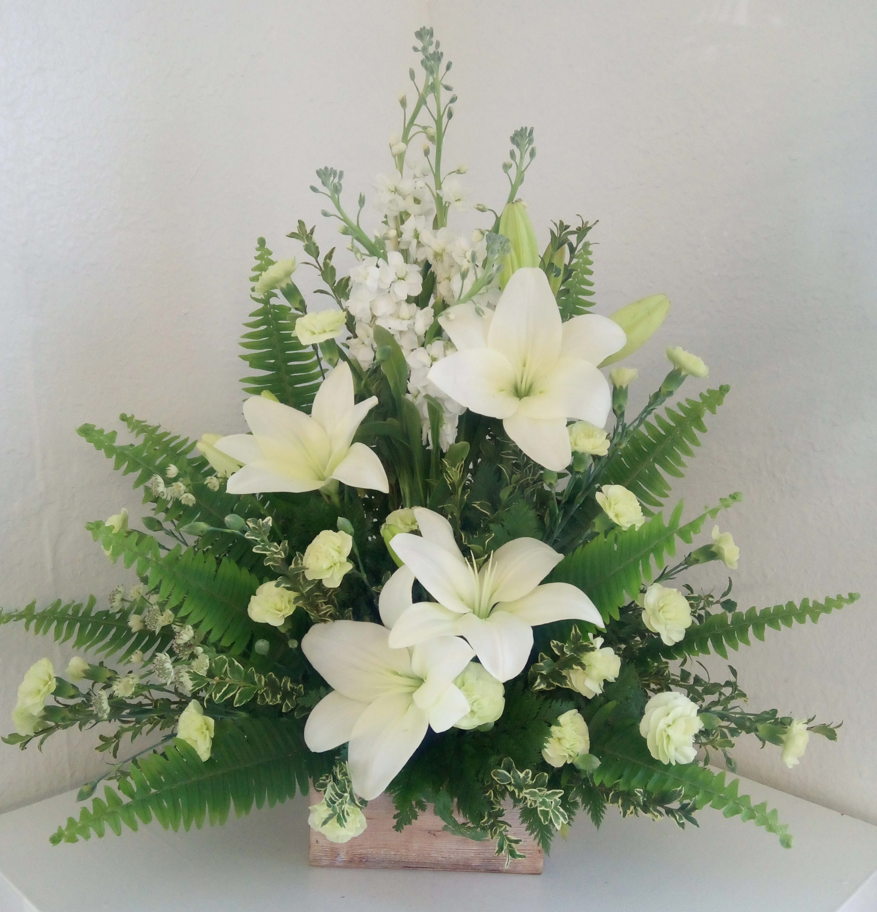 White lilies and small white flowers arranged in a wooden box with fern foliage