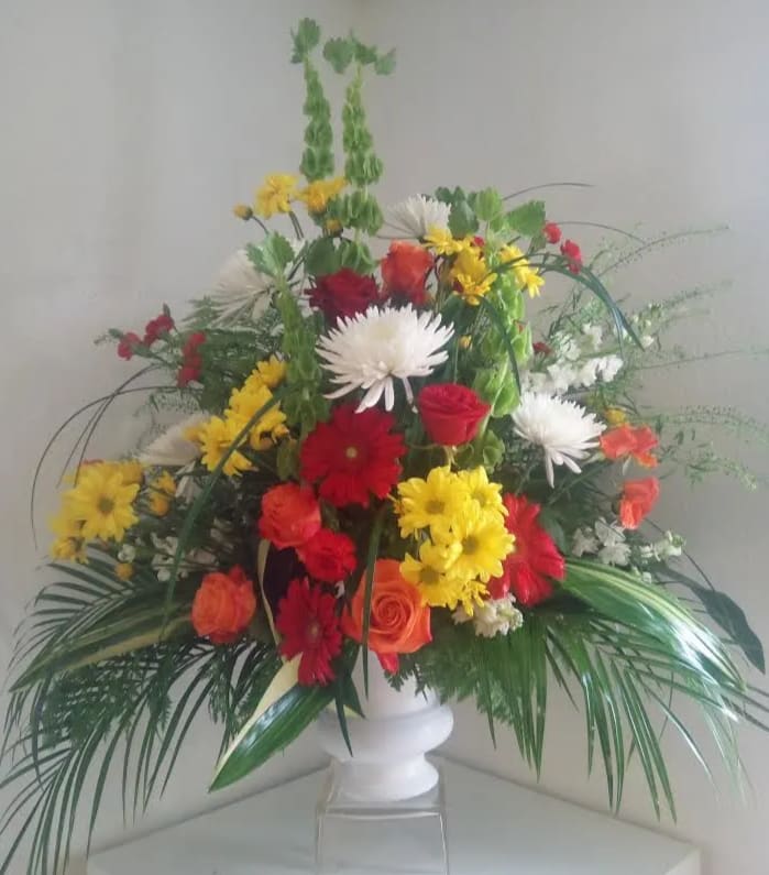 Mixed bouquet in a white pedestal vase with red, yellow, orange, and white flowers