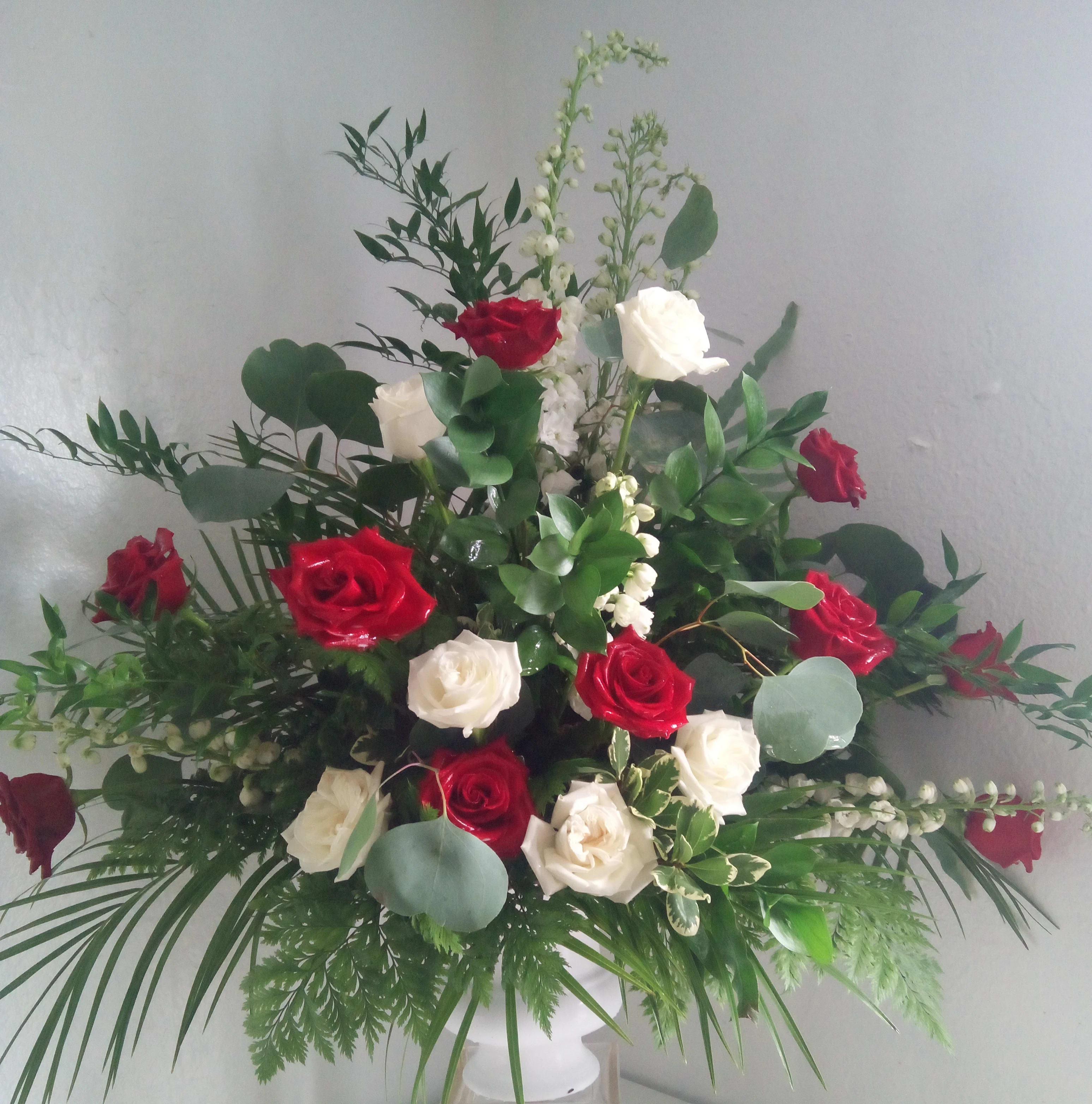 Red and white roses arranged in a tall vase with greenery