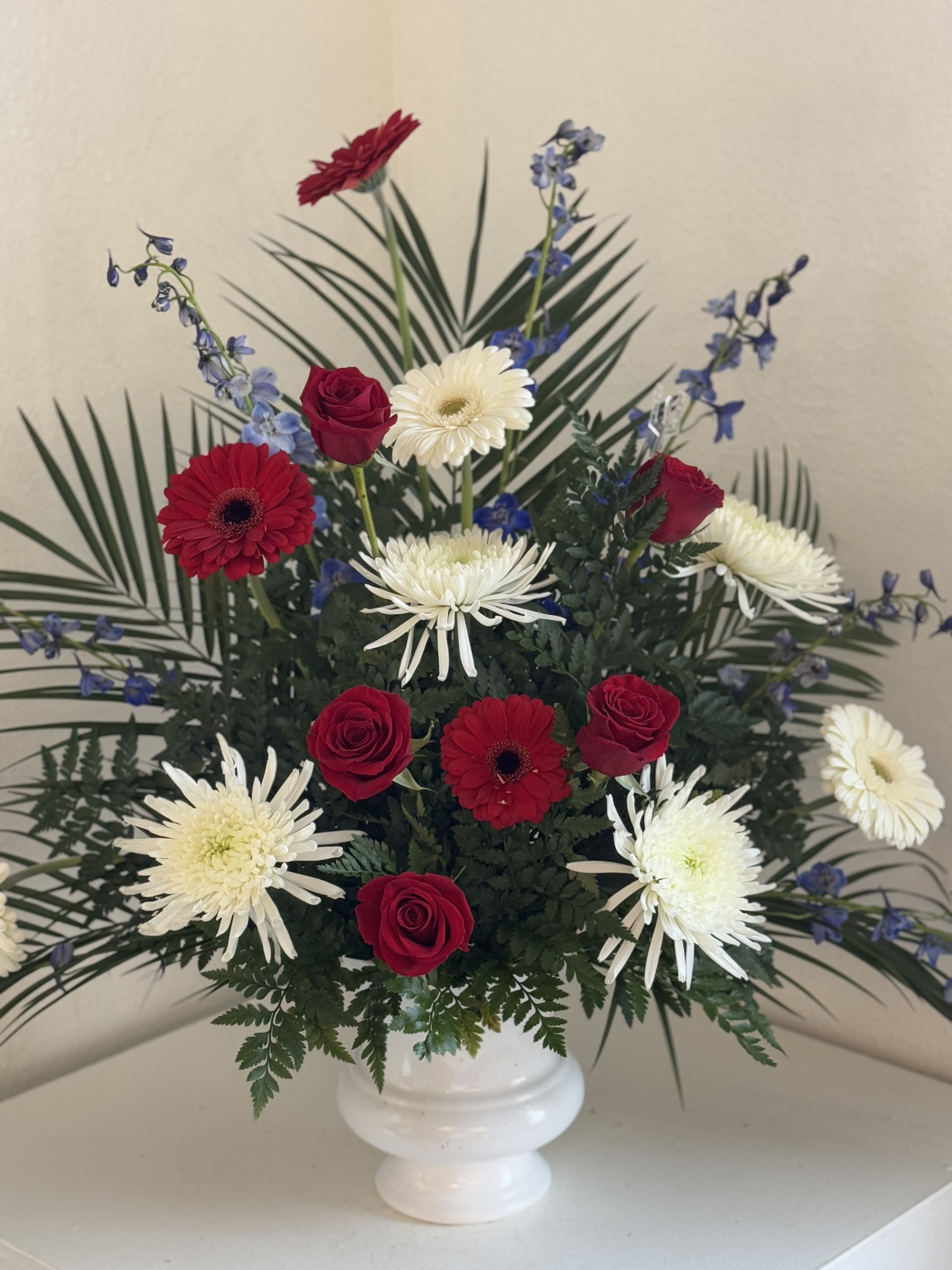 Red roses and white daisies in a white vase with blue accents