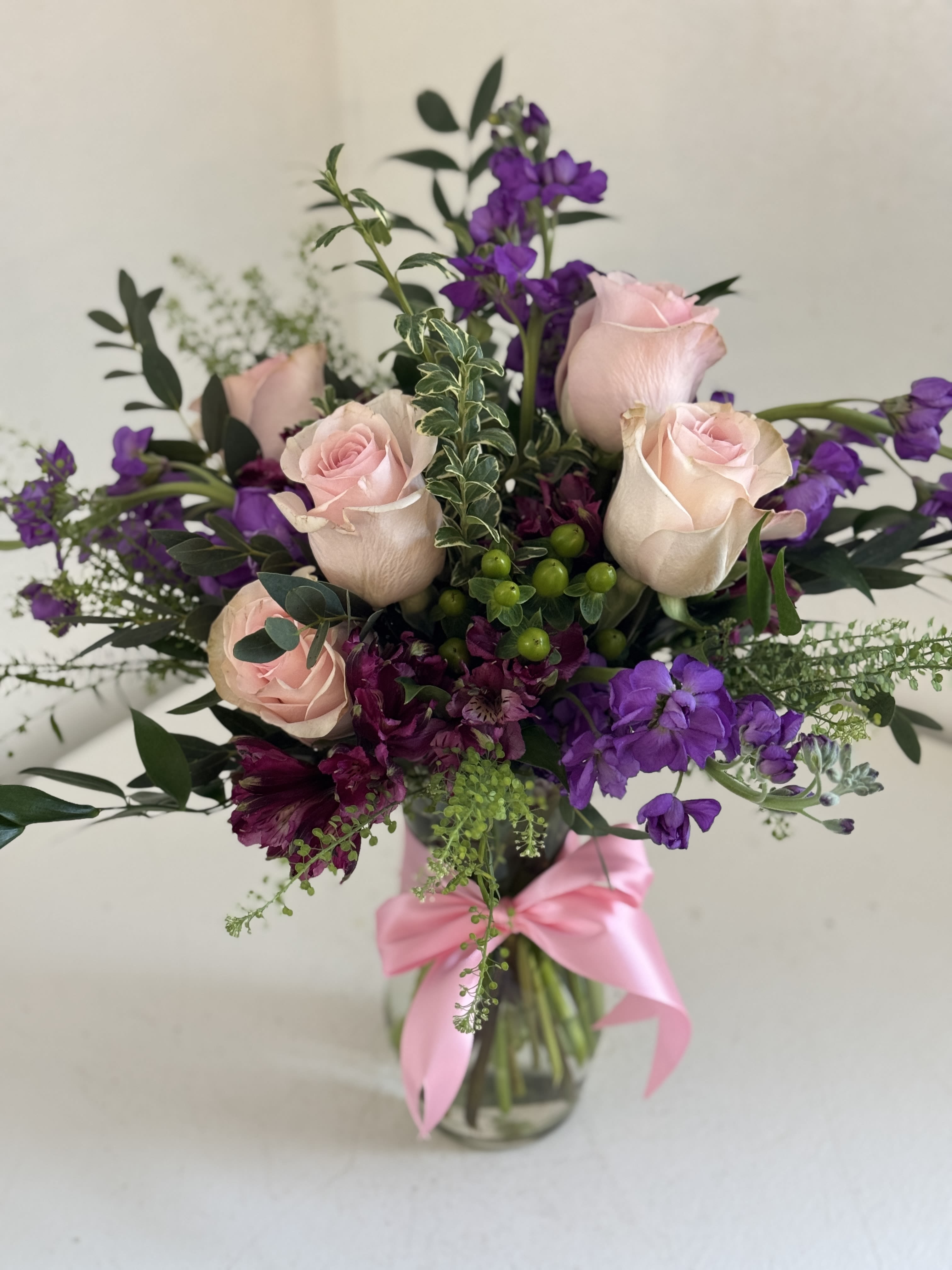 Vase of light pink roses with purple stock and alstroemeria, tied with a pink ribbon.