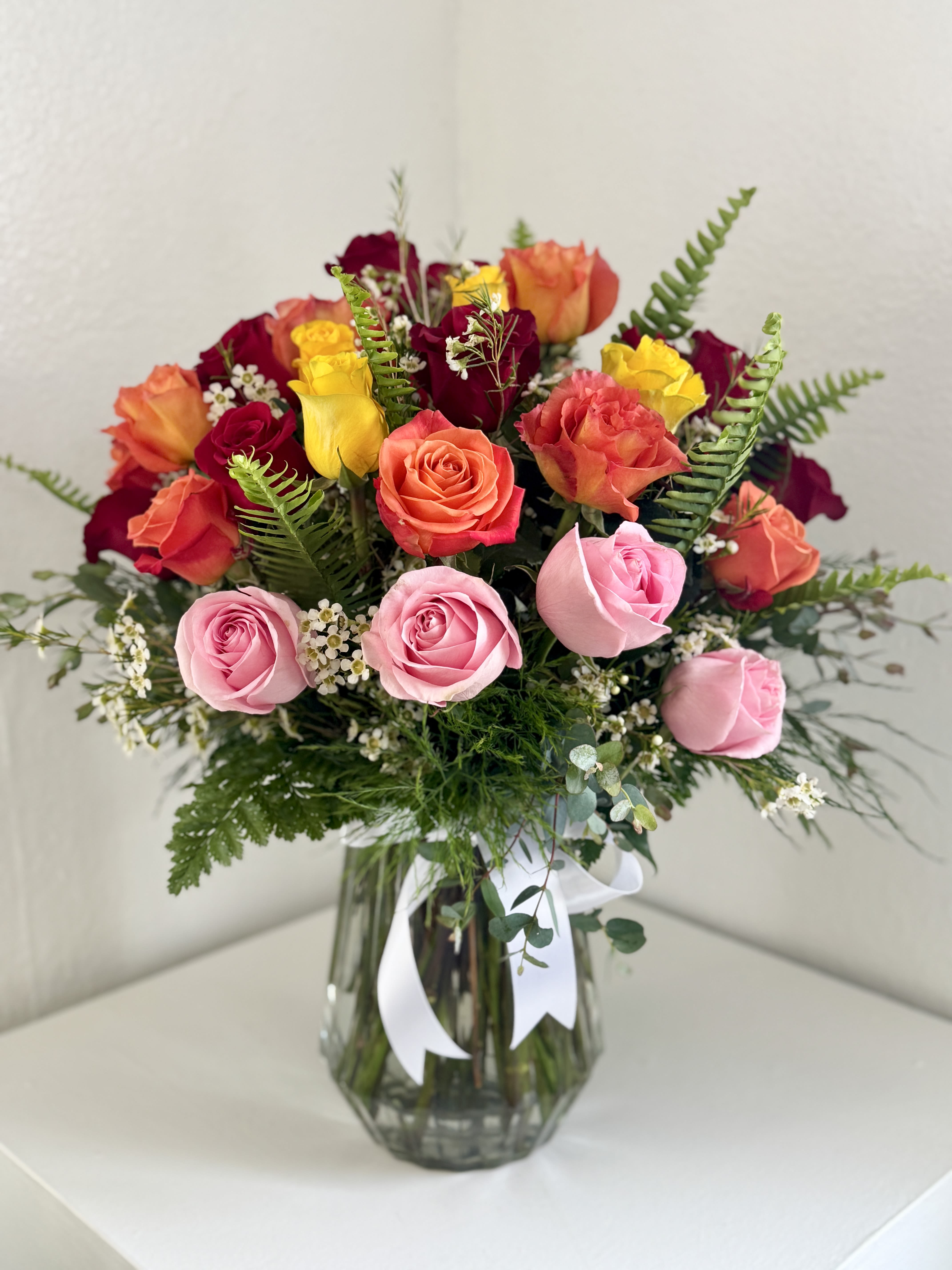Mixed roses in pink, coral, yellow, and burgundy in a glass vase