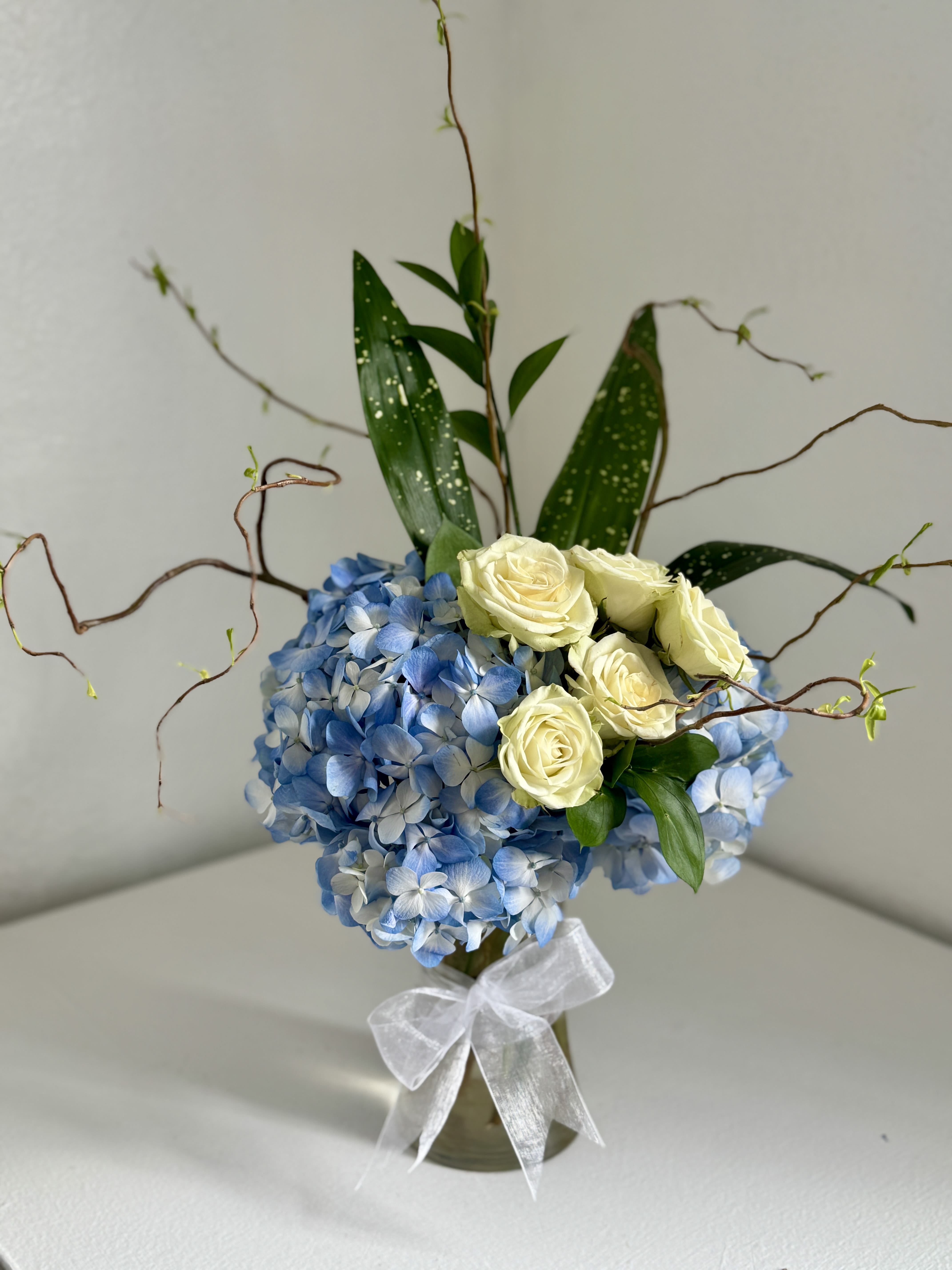 Blue hydrangea arrangement with cream roses in a glass vase