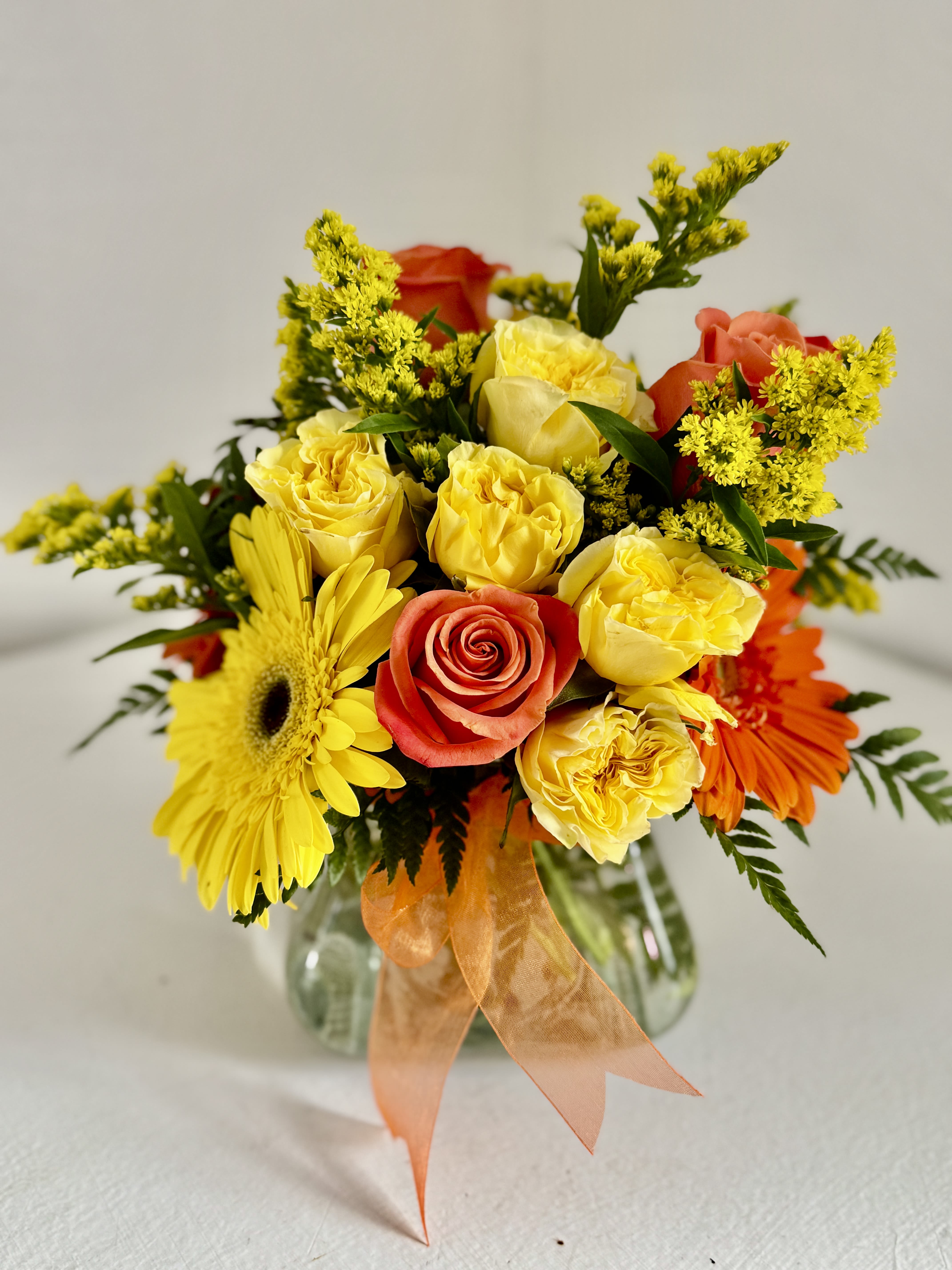 Mixed bouquet of yellow and orange flowers in a glass vase with an orange ribbon