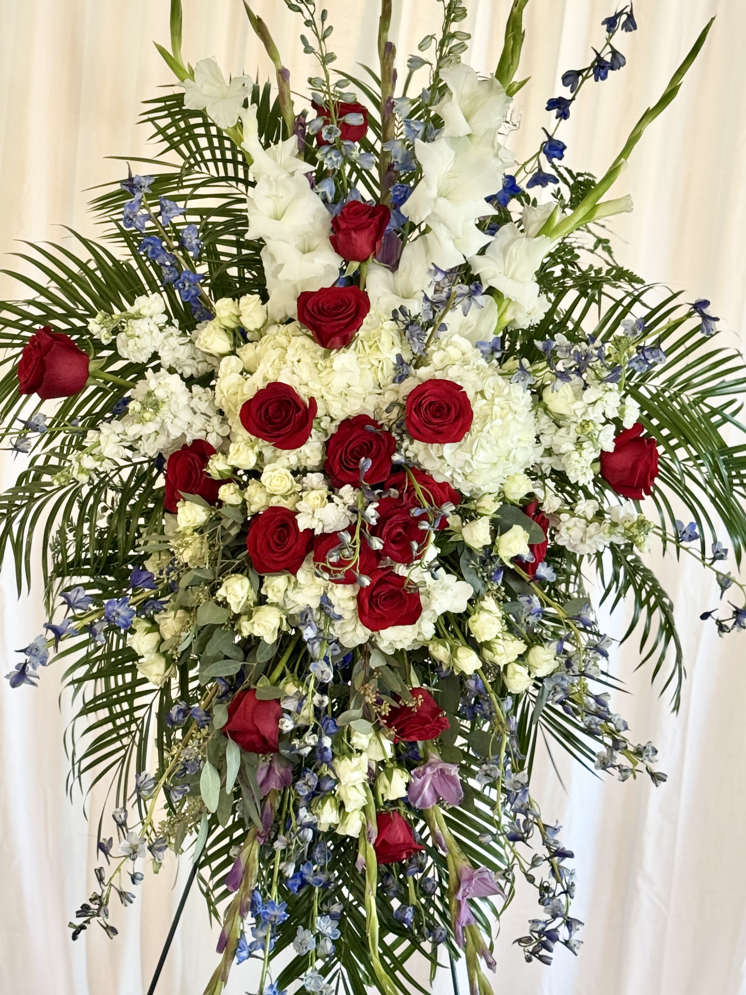 Tall floral standing spray with red roses, white blooms, and blue accents