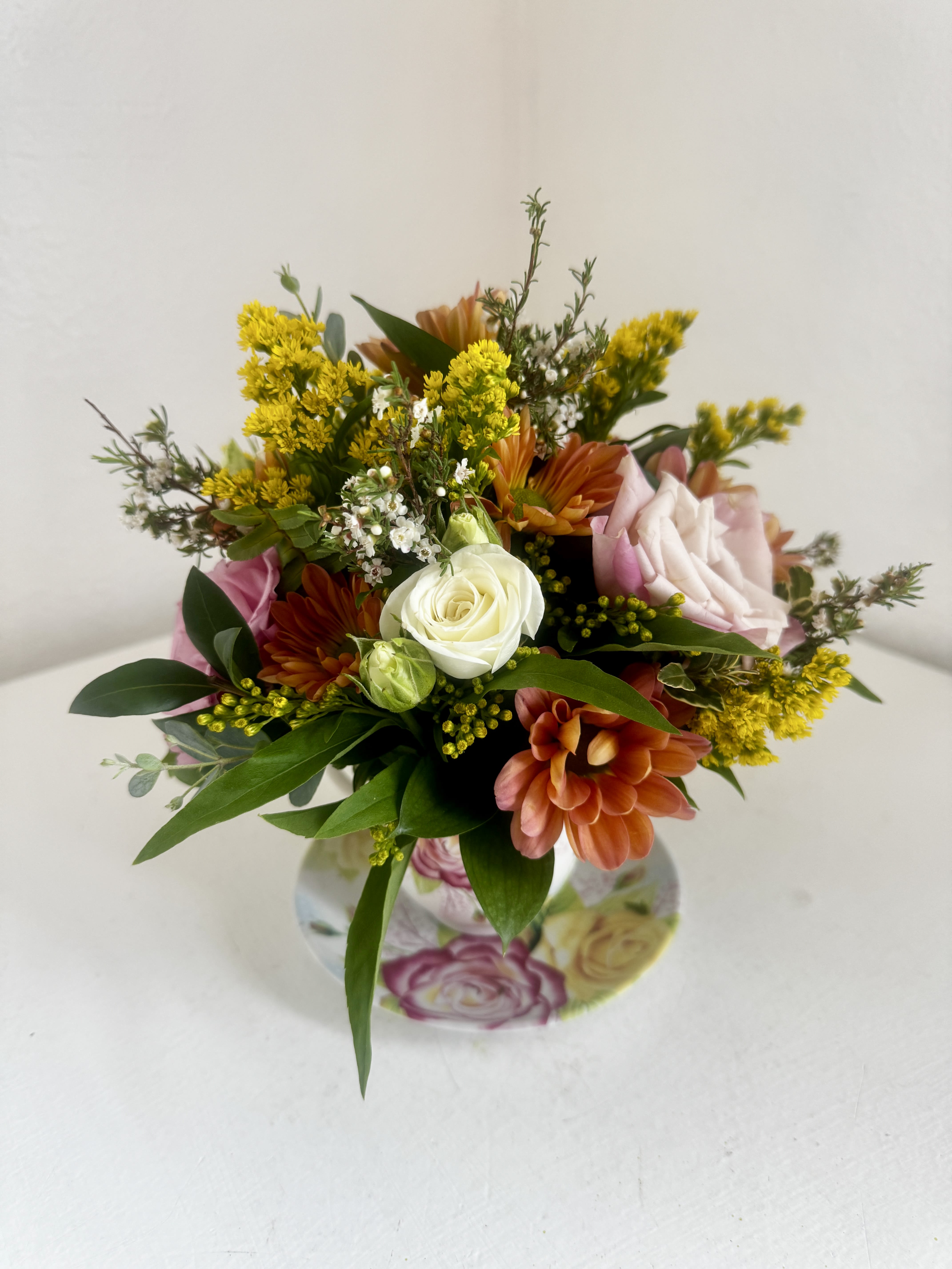Mixed bouquet with white and pink roses, orange blooms, and yellow filler flowers in a floral vase