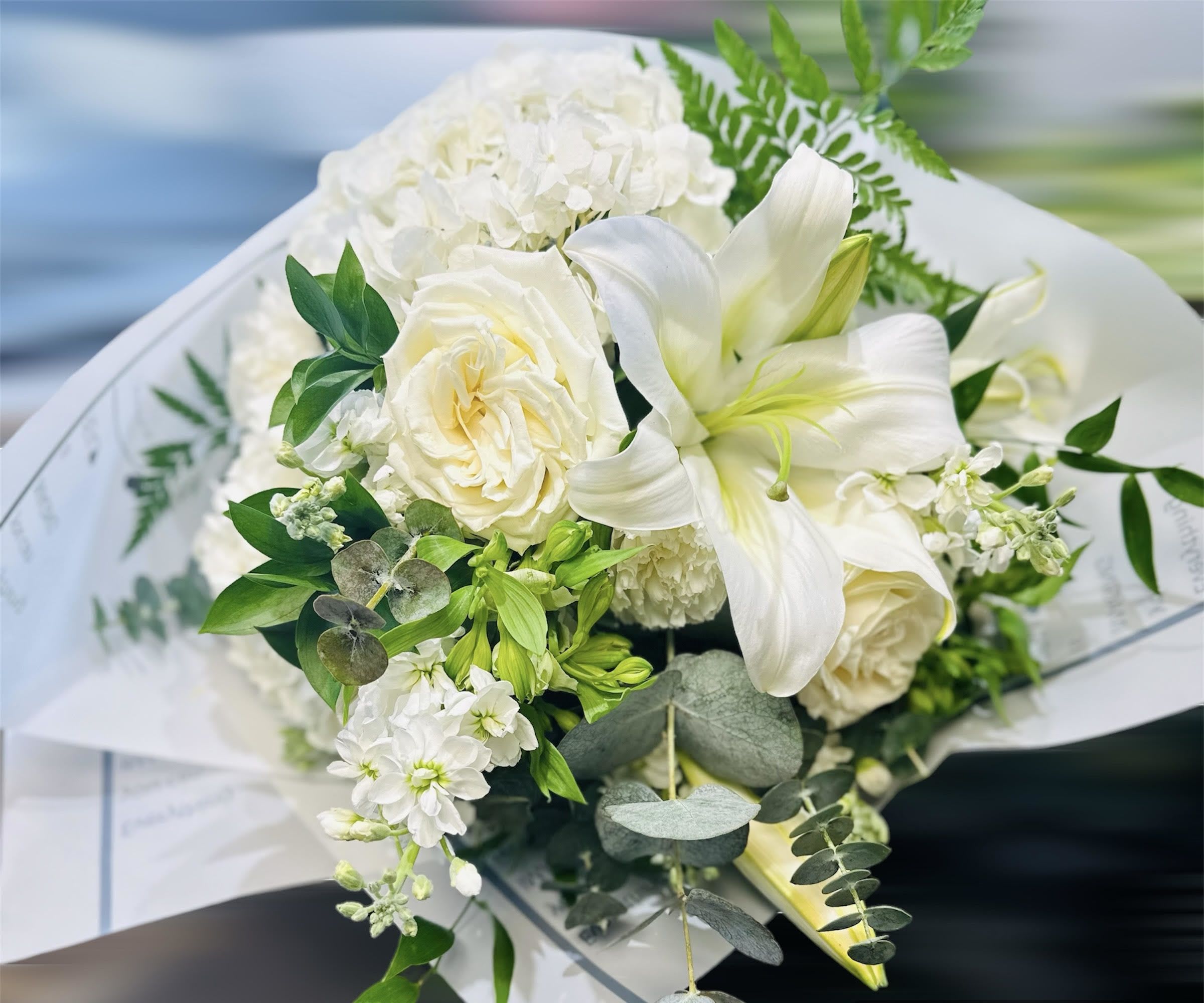 White bouquet with lilies, roses, and hydrangea wrapped in paper