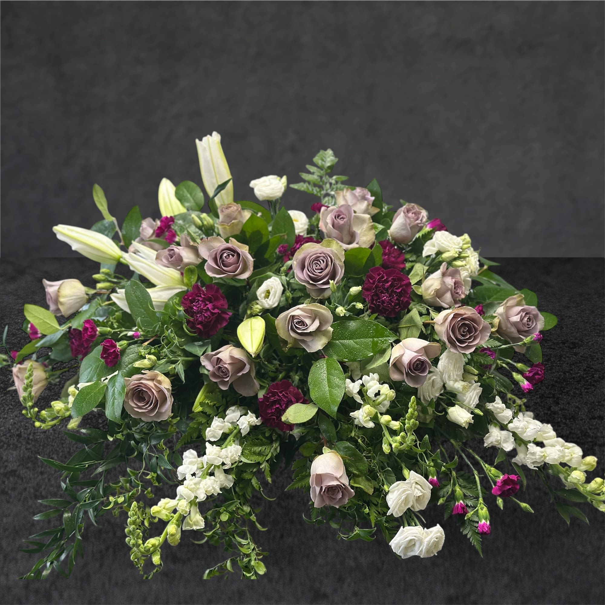 Low floral arrangement with mauve roses, white lilies, and burgundy accents