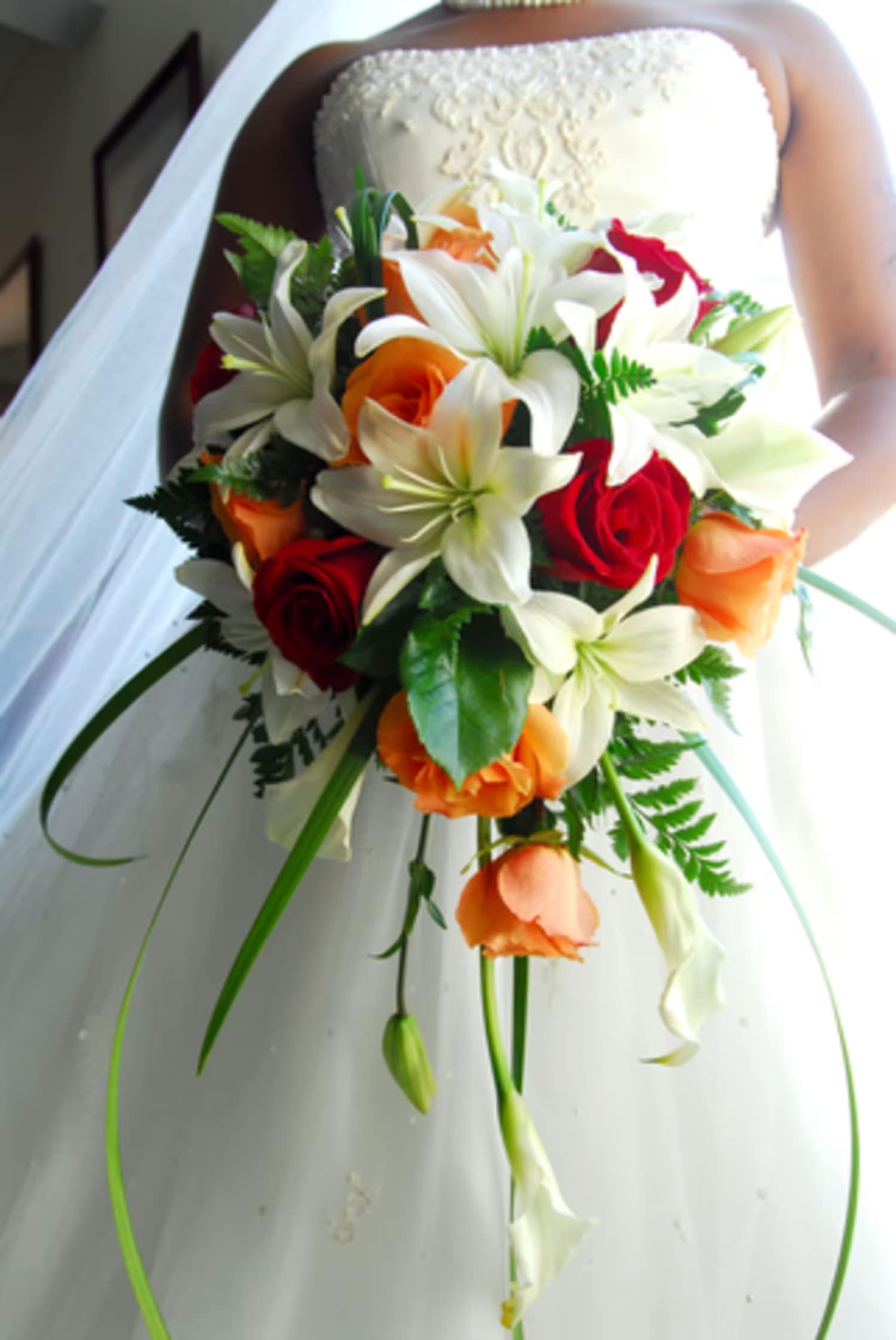 Bride holding a bouquet of white lilies, red and orange roses