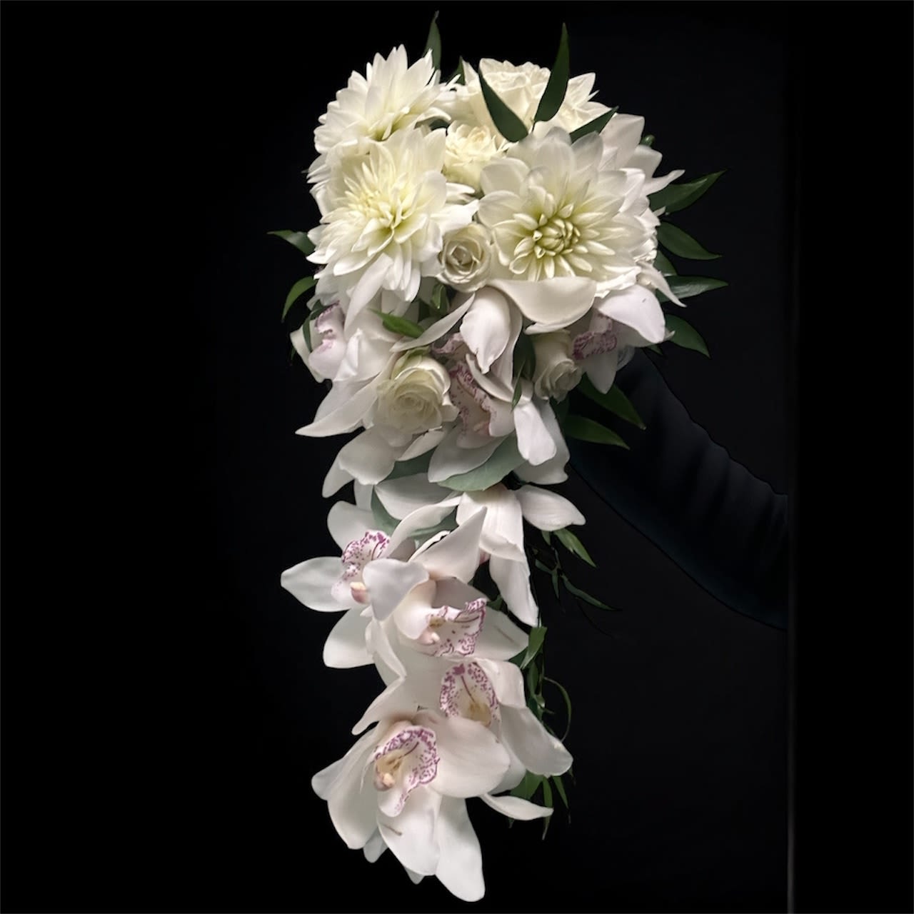 White cascading bouquet with orchids and dahlias against a black background