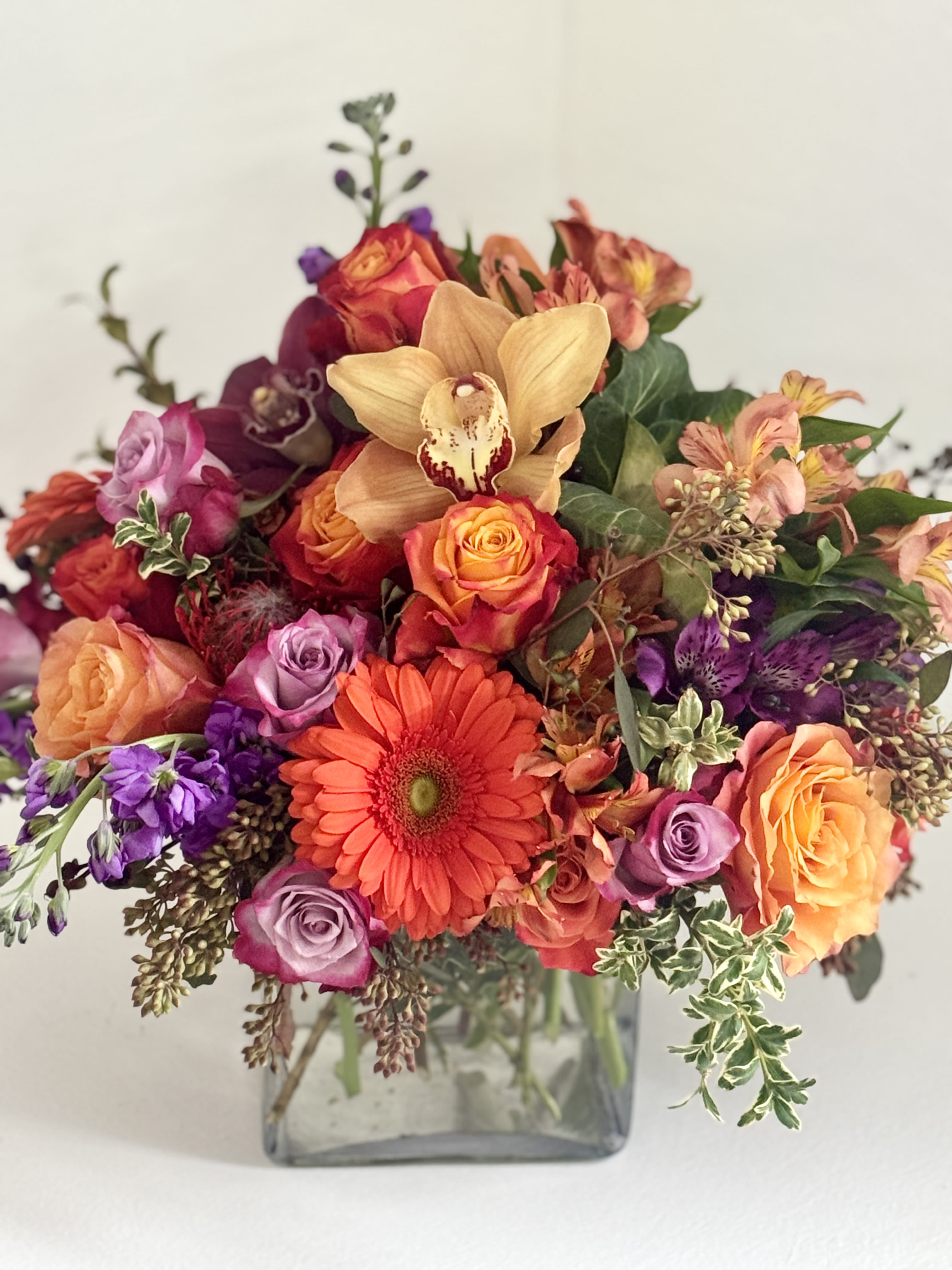 Mixed bouquet of roses, gerbera daisies, and orchids in a glass vase