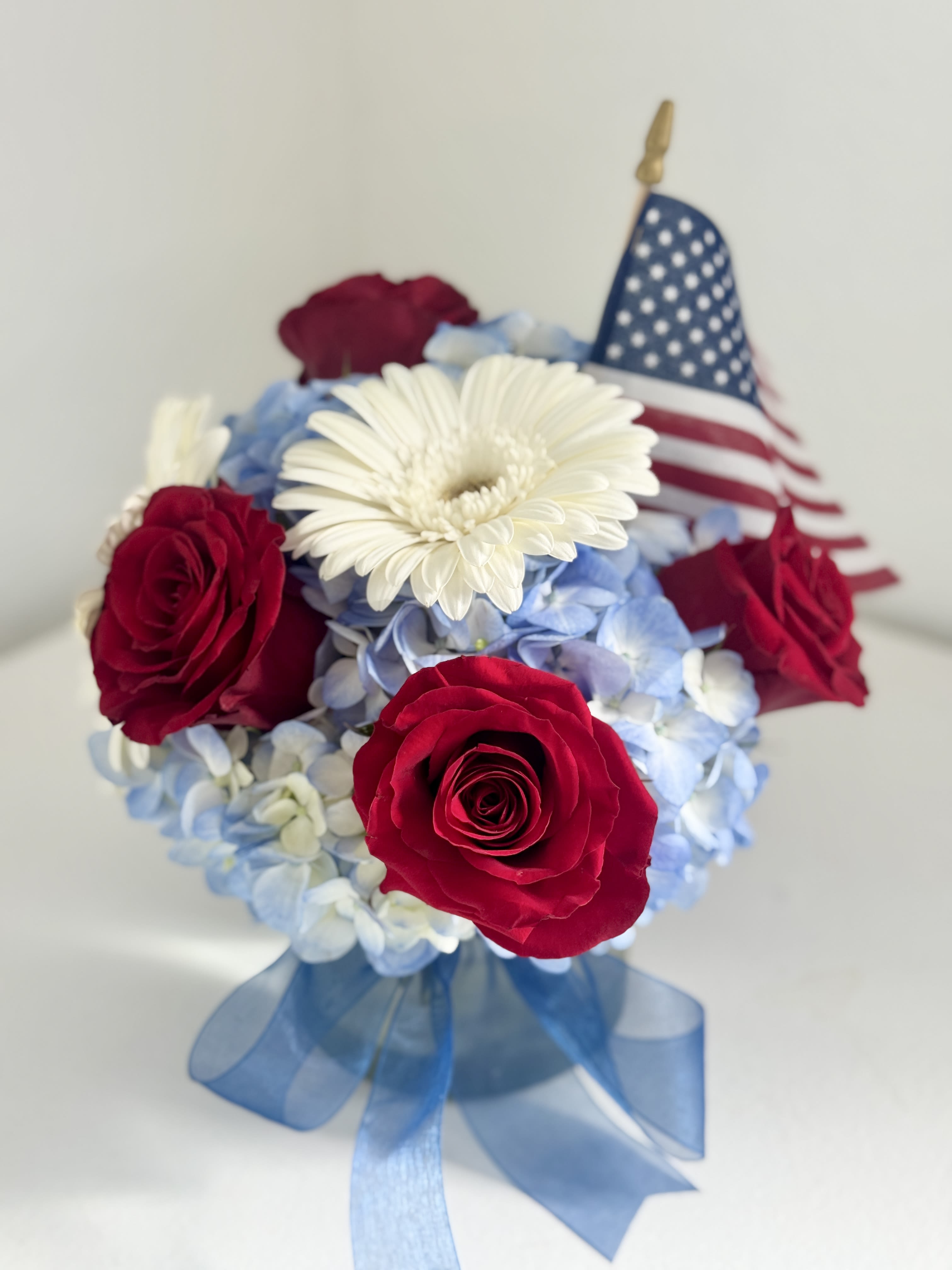 Red roses and white daisy bouquet with a small American flag