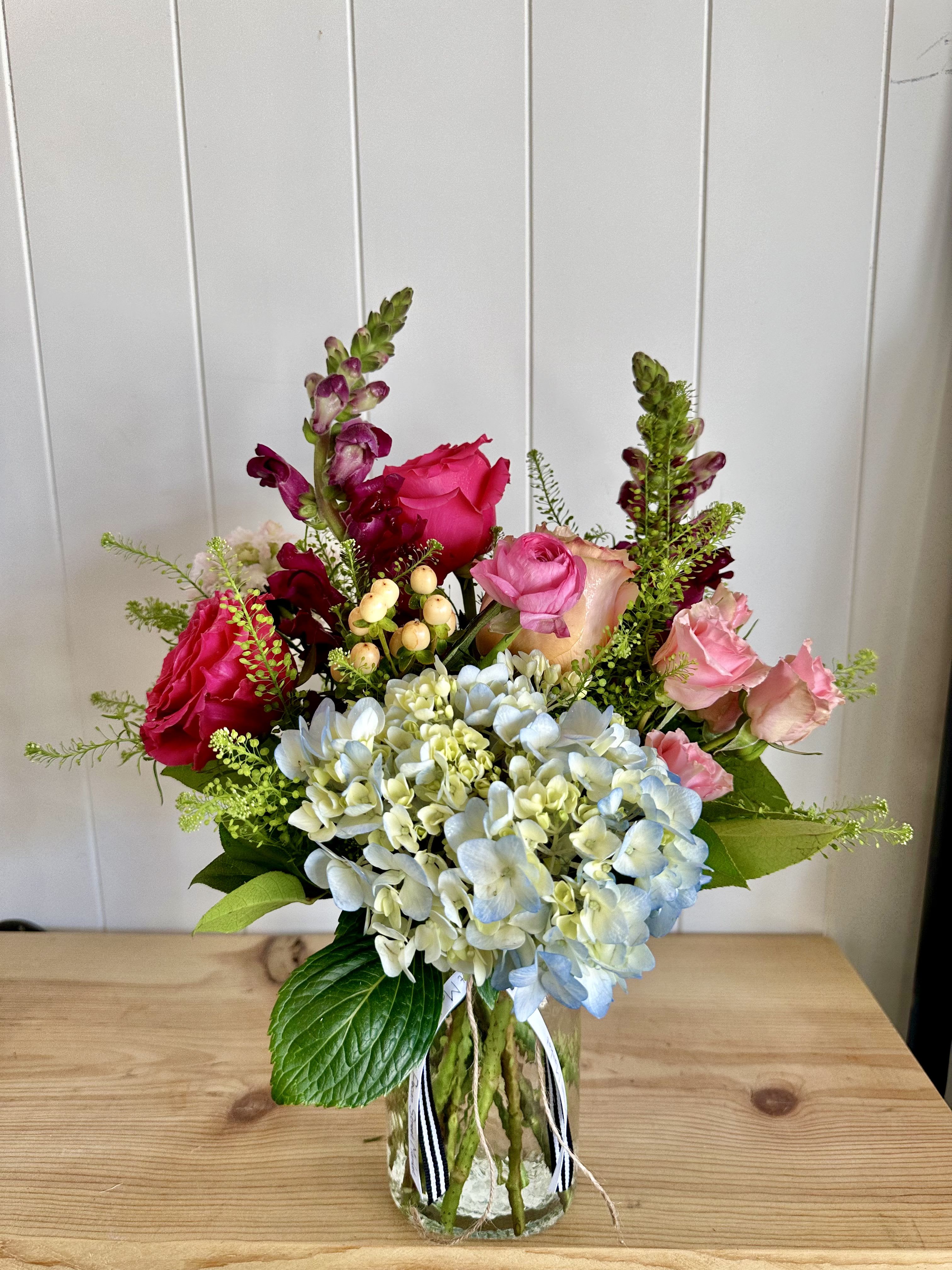 Mixed bouquet of roses, hydrangeas, and snapdragons in a glass vase