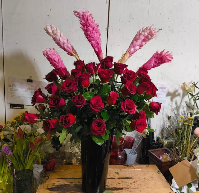 Tall arrangement of red roses with pink spiked tropical flowers in a glossy black vase