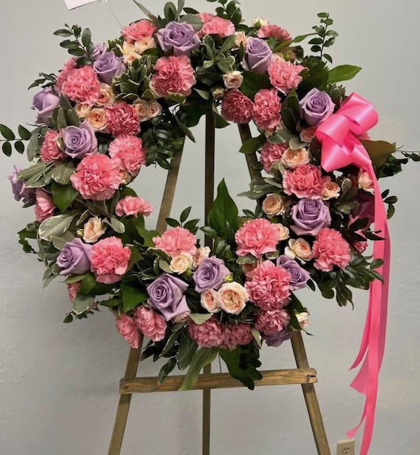 Standing wreath of pink carnations and lavender roses with a pink bow on a wooden easel