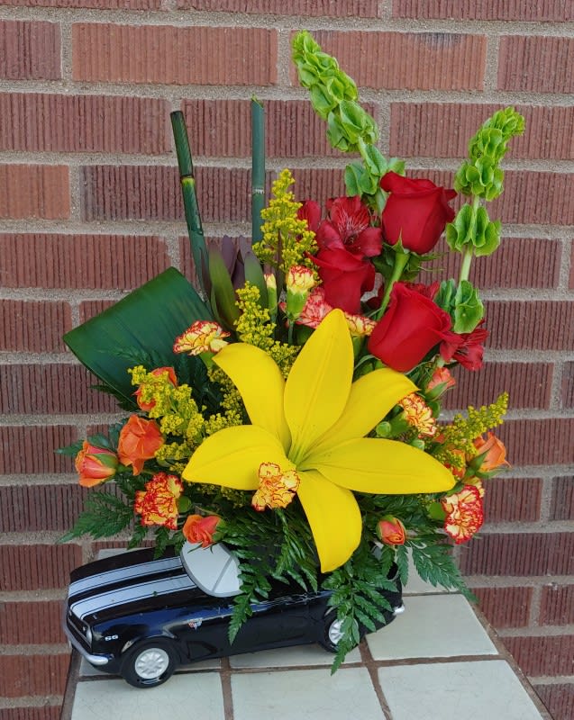 Floral arrangement in a toy car with red roses and a large yellow lily