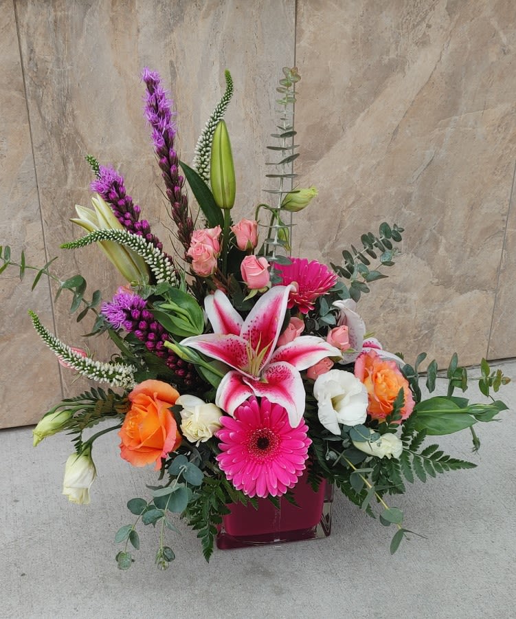 Mixed bouquet with pink lilies, roses, and gerbera daisies in a square vase