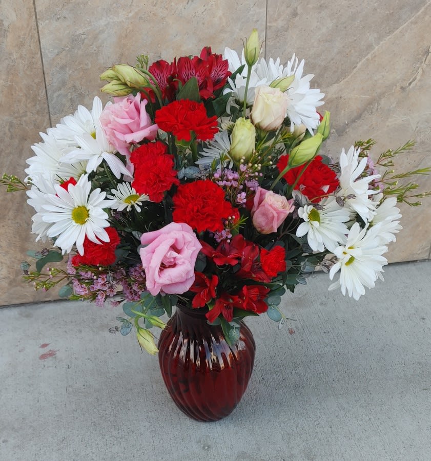 Bouquet of red and pink flowers with white daisies in a red glass vase
