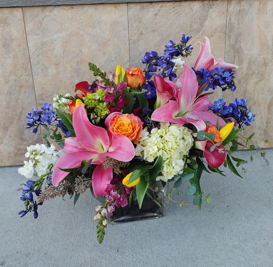 Mixed bouquet with pink lilies, roses, and blue flowers in a glass vase