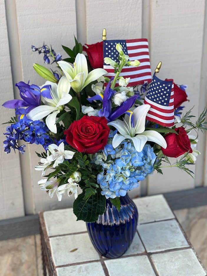 Red roses and white lilies in a blue vase with small American flags