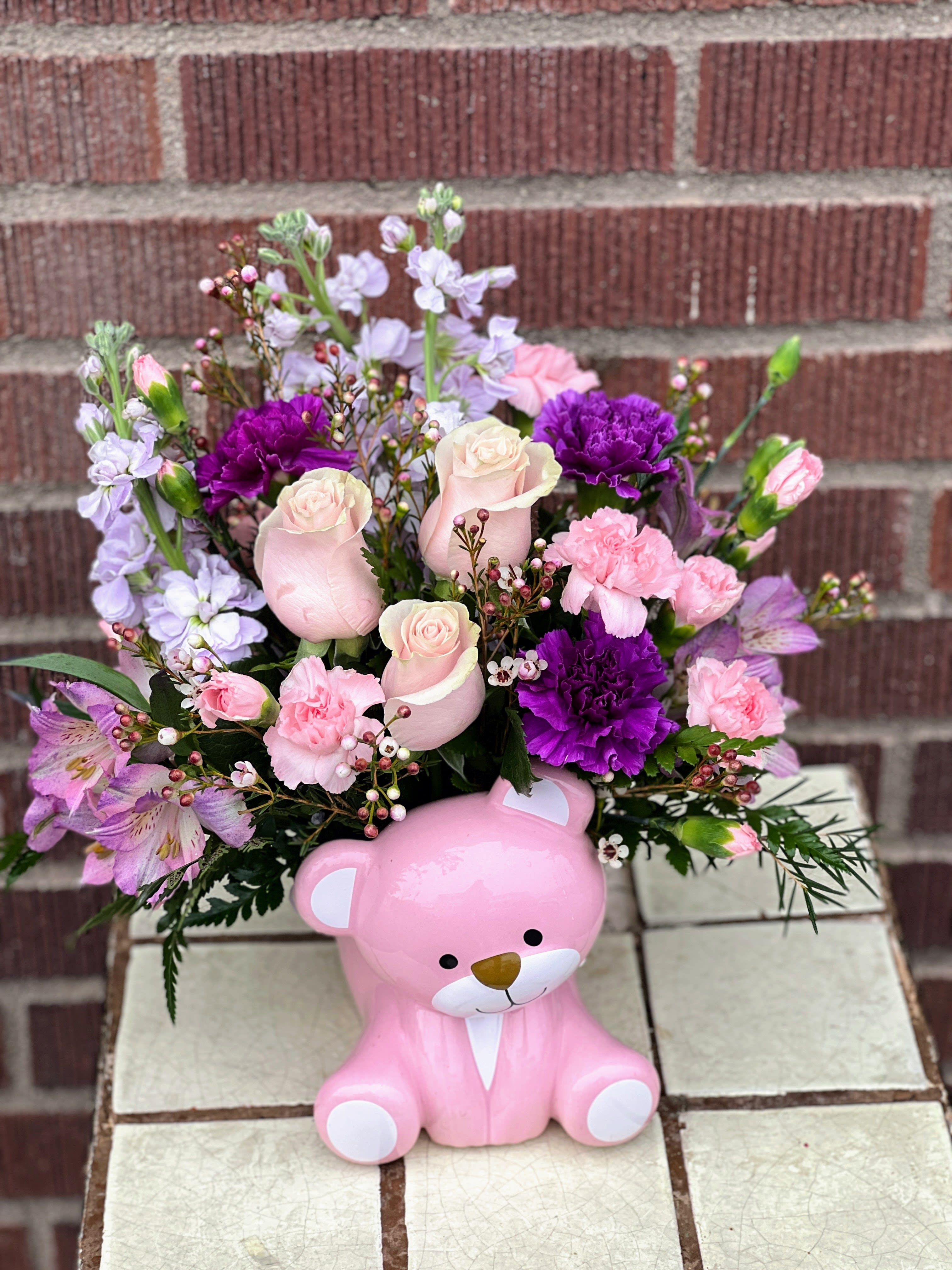 Pink teddy bear container holding a mixed bouquet of roses and carnations
